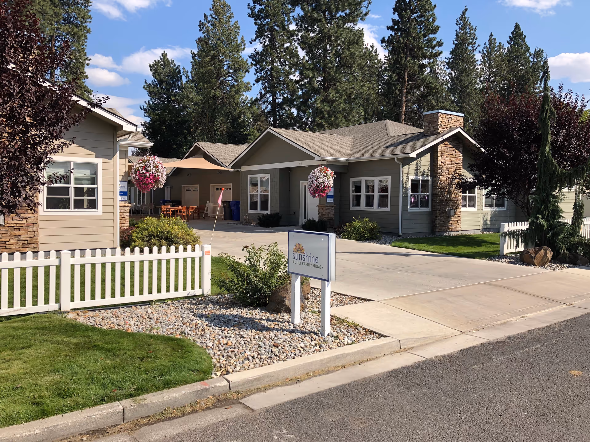 Single-story Sunshine Adult Family Homes front exterior with sign, white fence, and landscaped entrance.
