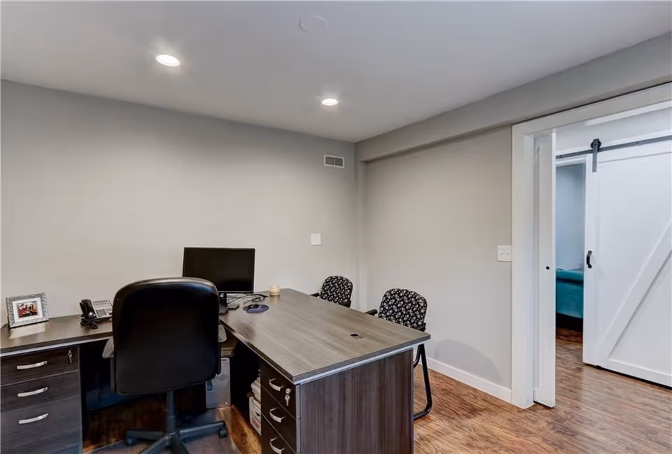 Office desk with computer and two patterned chairs in a neutral, well-lit room.