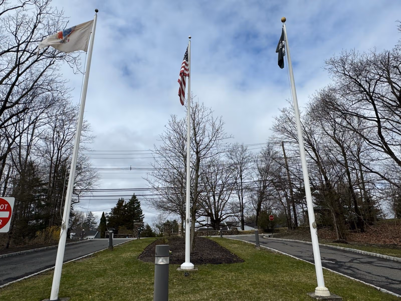 Three flagpoles with flags flank a circular entrance driveway and leafless trees.