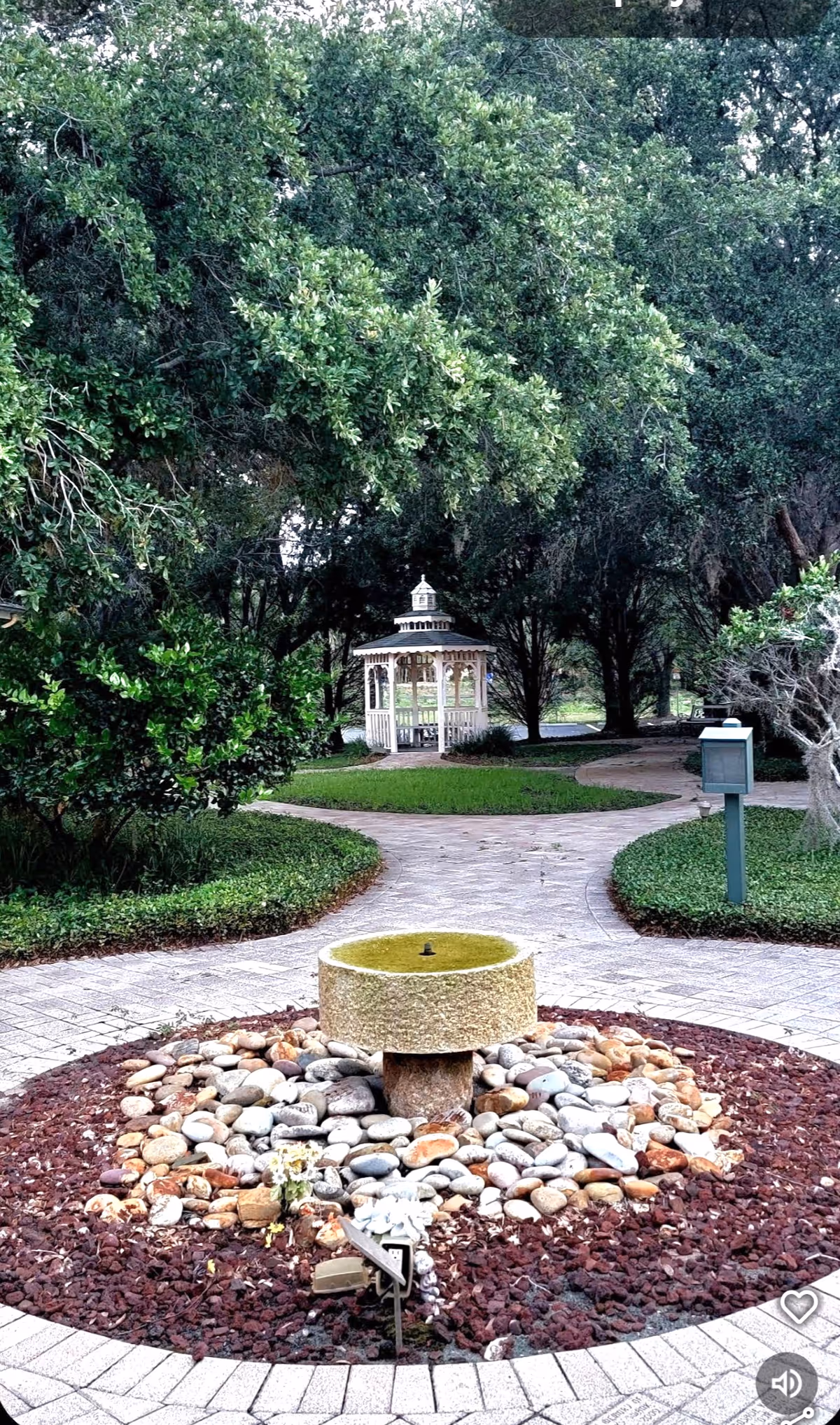 Stone path winds through a garden toward a white gazebo and fountain.