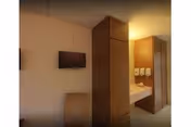Wooden cabinets flank a corridor with a wall-mounted TV in a senior living facility.