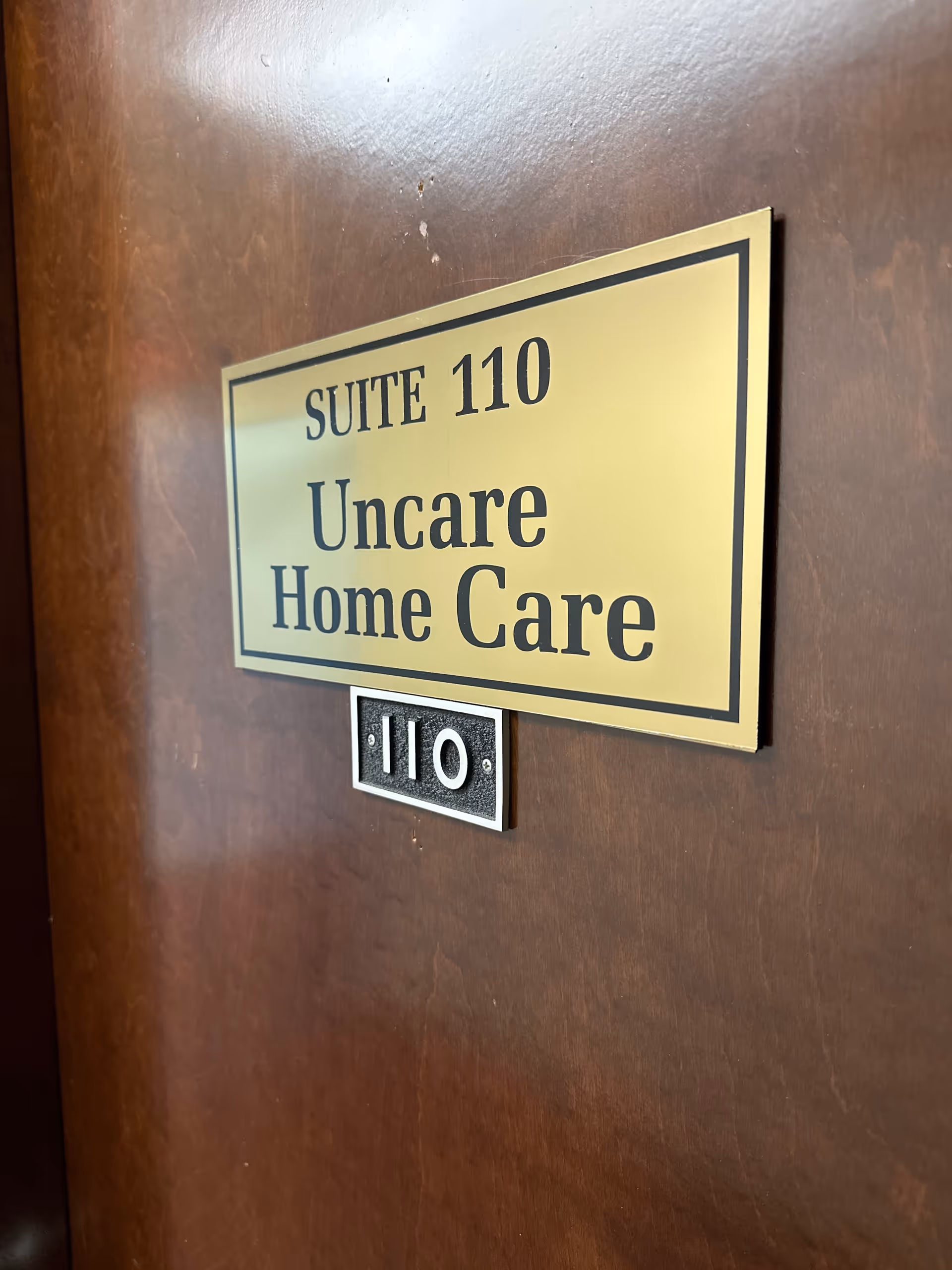 Gold plaque on a wooden door reads Suite 110 Uncare Home Care.