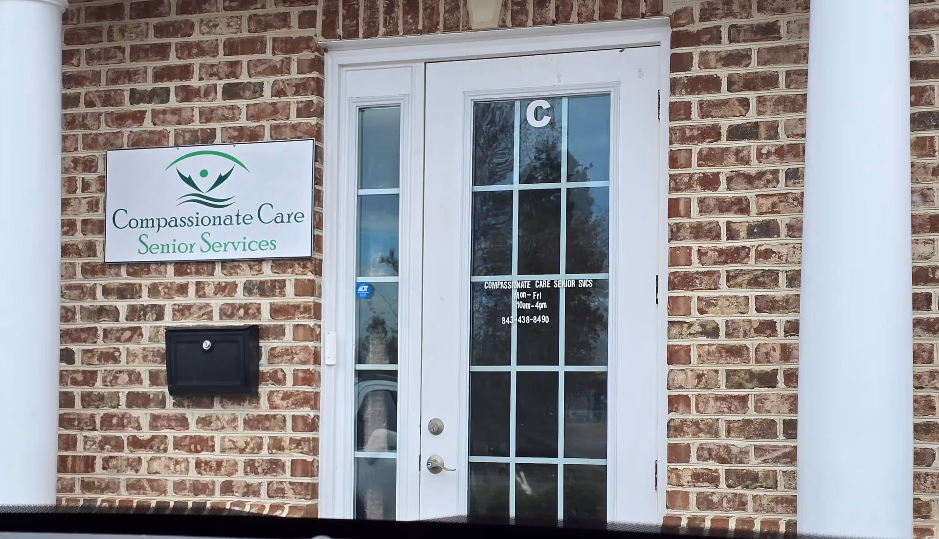 Brick building entrance with a glass door and Compassionate Care Senior Services sign.