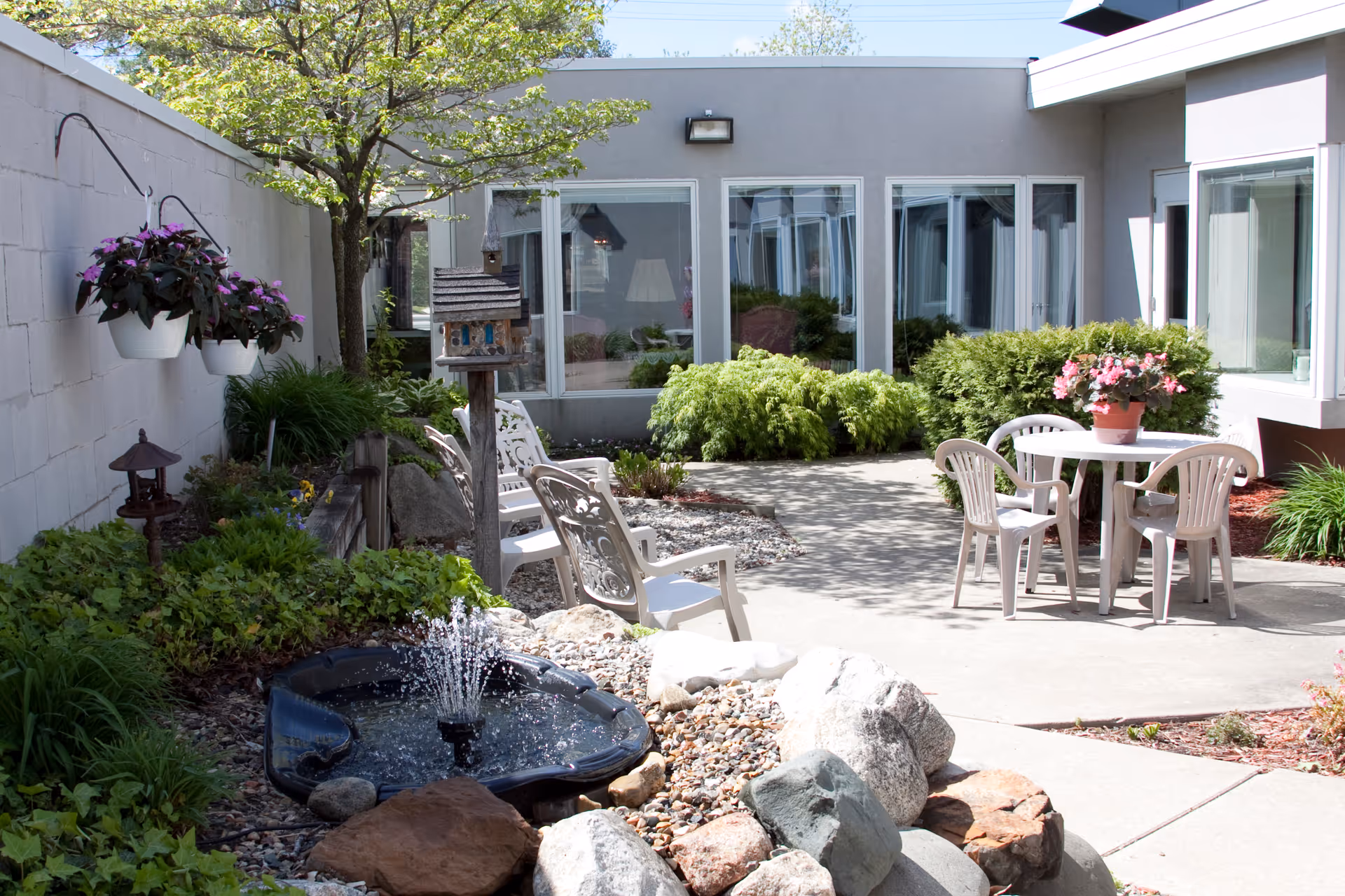 Landscaped courtyard with a patio table and chairs, a small fountain, planters and windows of the facility.