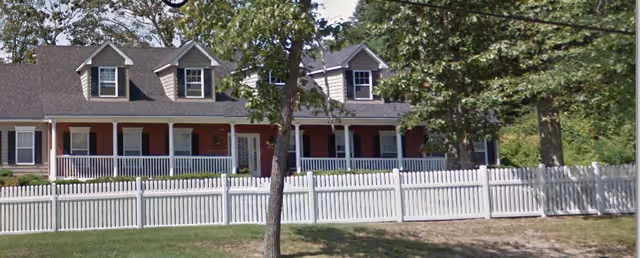 Exterior view of Millennium Memory Care at Ocean with a white picket fence and trees.