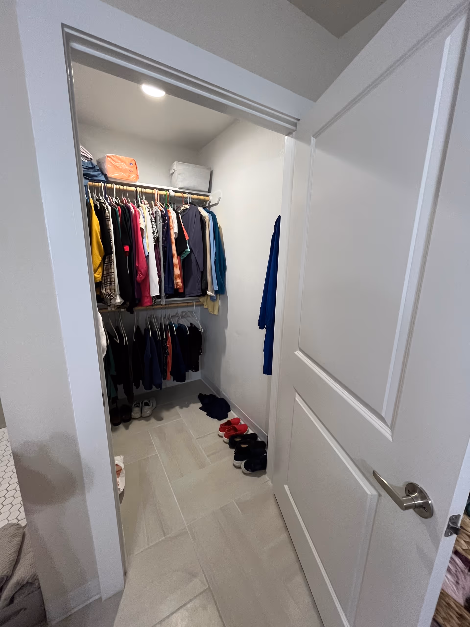 Open closet with clothes hanging, shelves, and slippers on tiled floor.