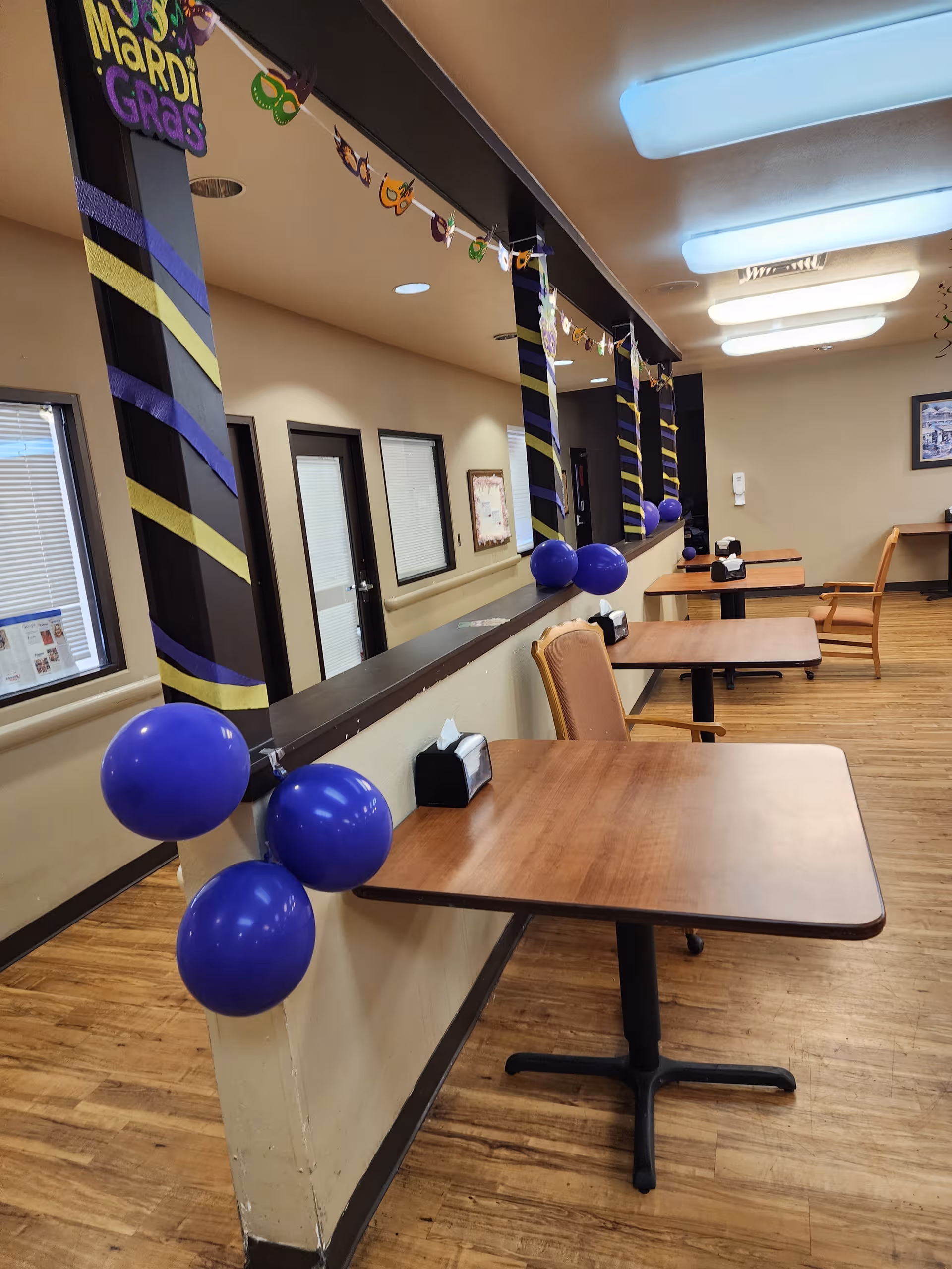 Indoor dining area in a senior facility decorated with Mardi Gras balloons.