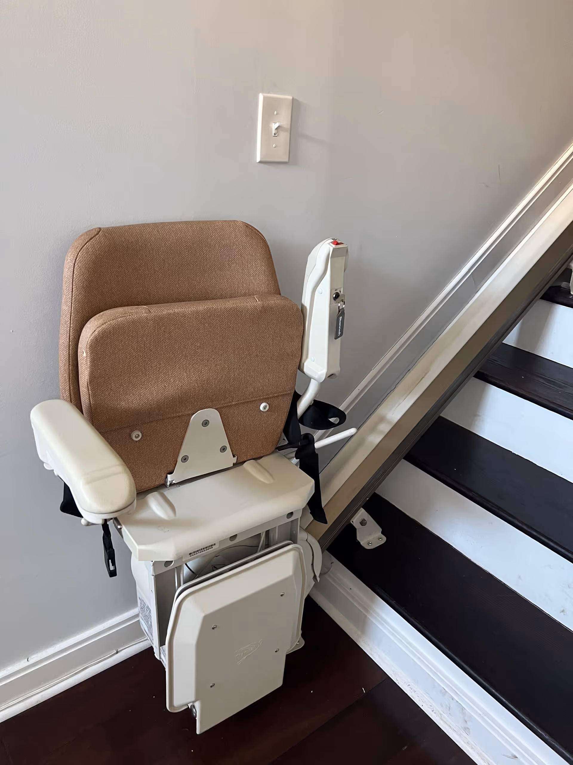 A beige stair lift chair installed beside a staircase in a senior living facility interior.