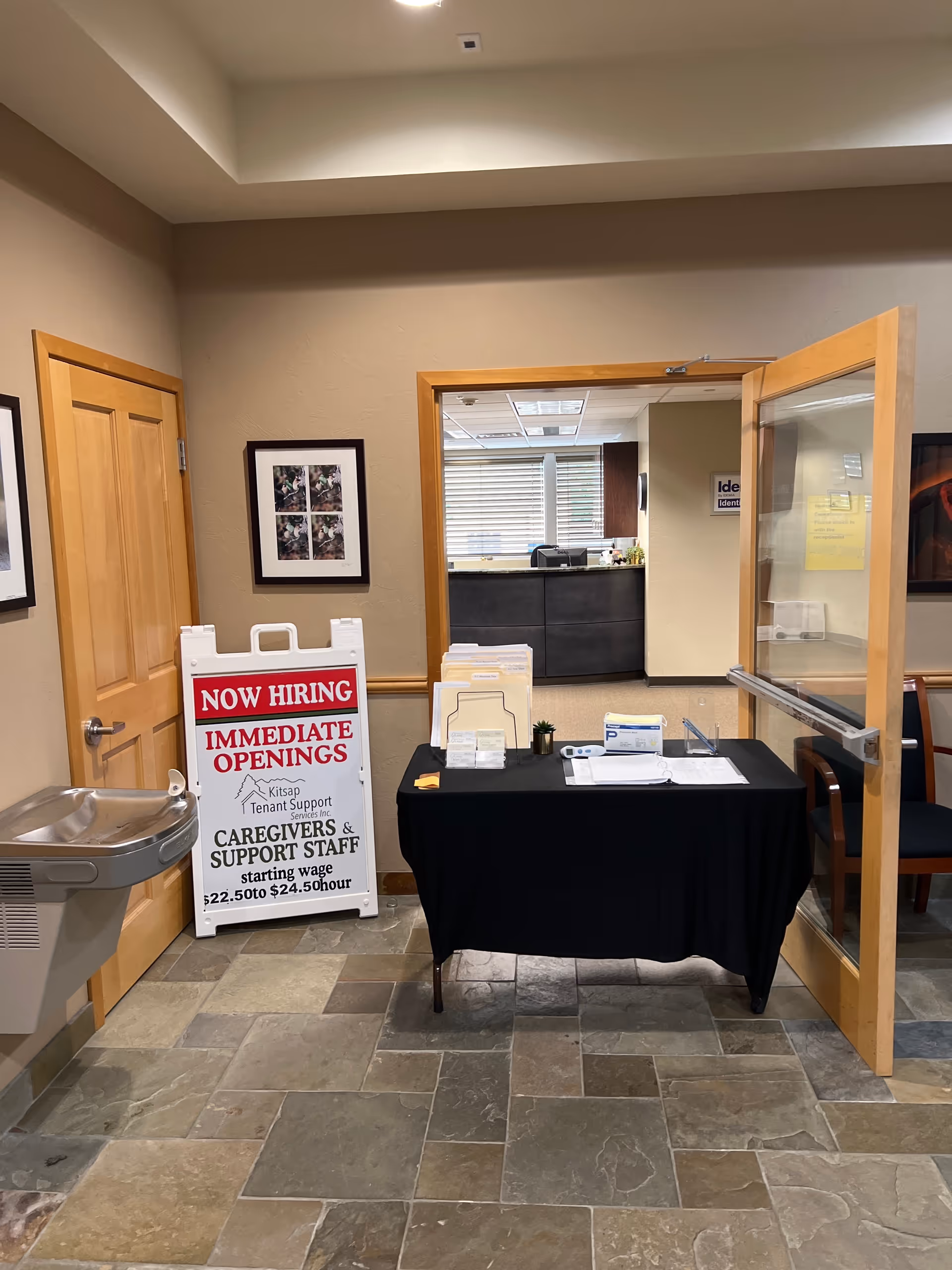 Interior lobby with a desk, doorway to reception, and a now-hiring sign.