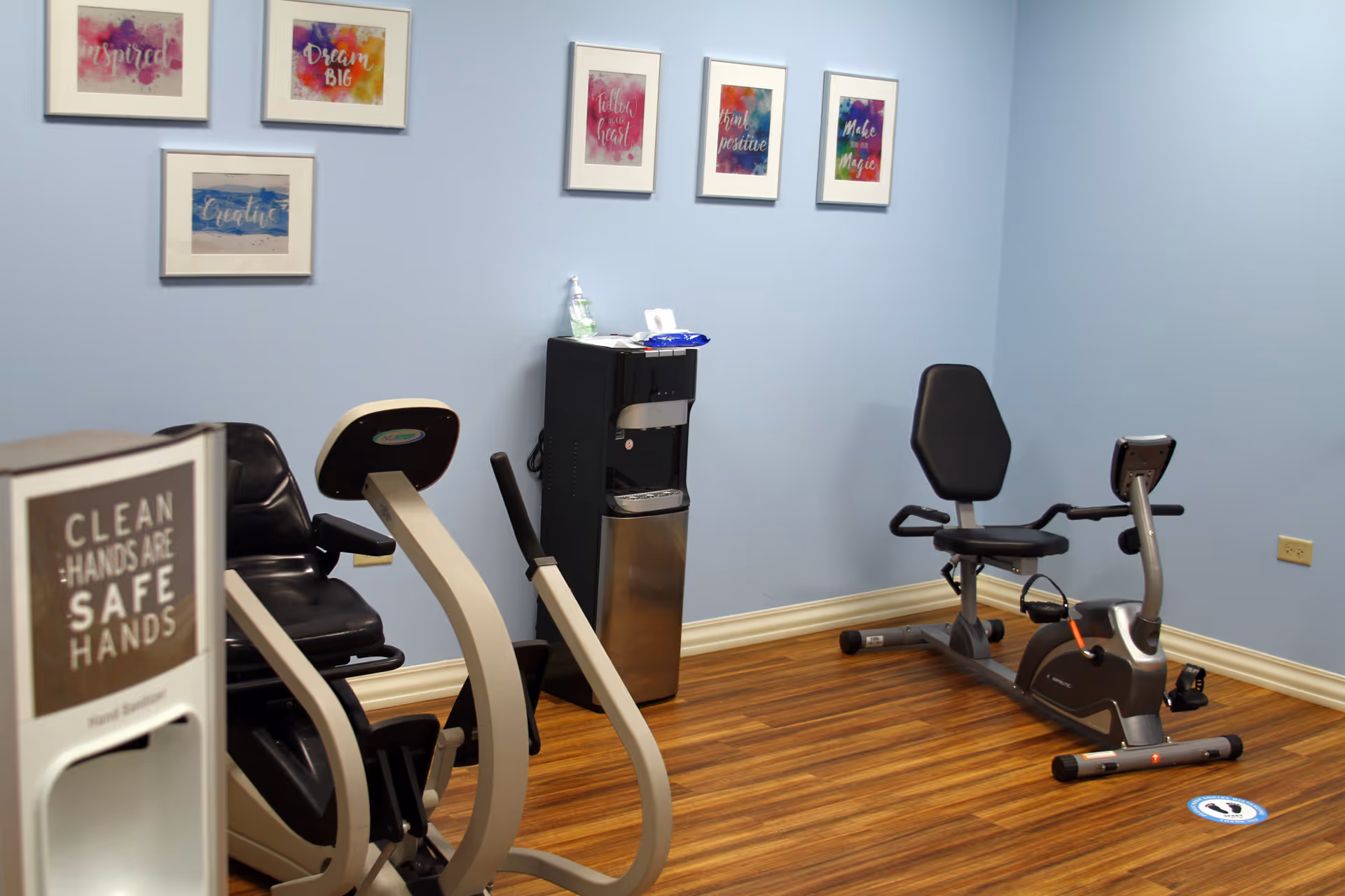 A small indoor fitness room with exercise bikes, a water cooler, and wall art.