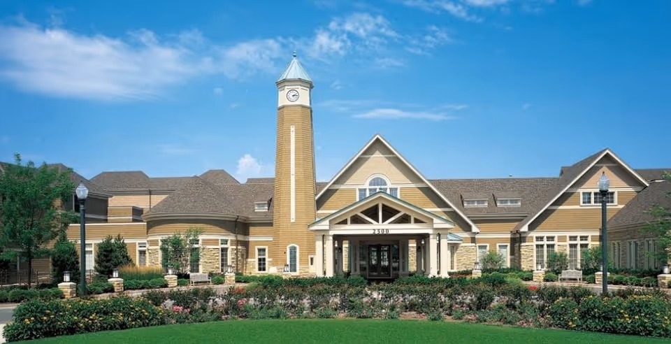 Exterior view of a senior living facility with a clock tower and landscaped entrance.