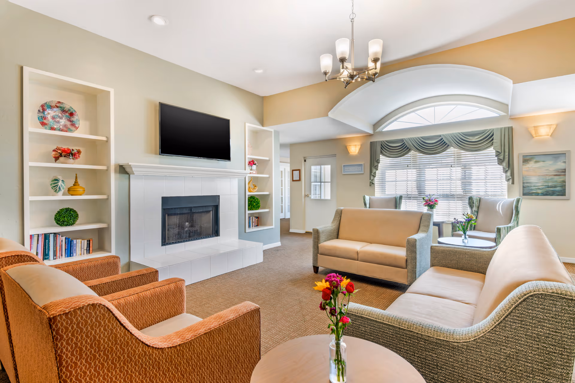 Bright senior living lounge with sofas, fireplace, and TV.