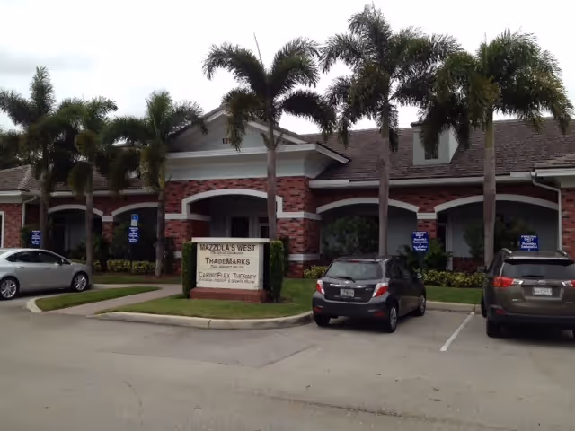 Brick senior facility facade with arches, palm trees, and parked cars.