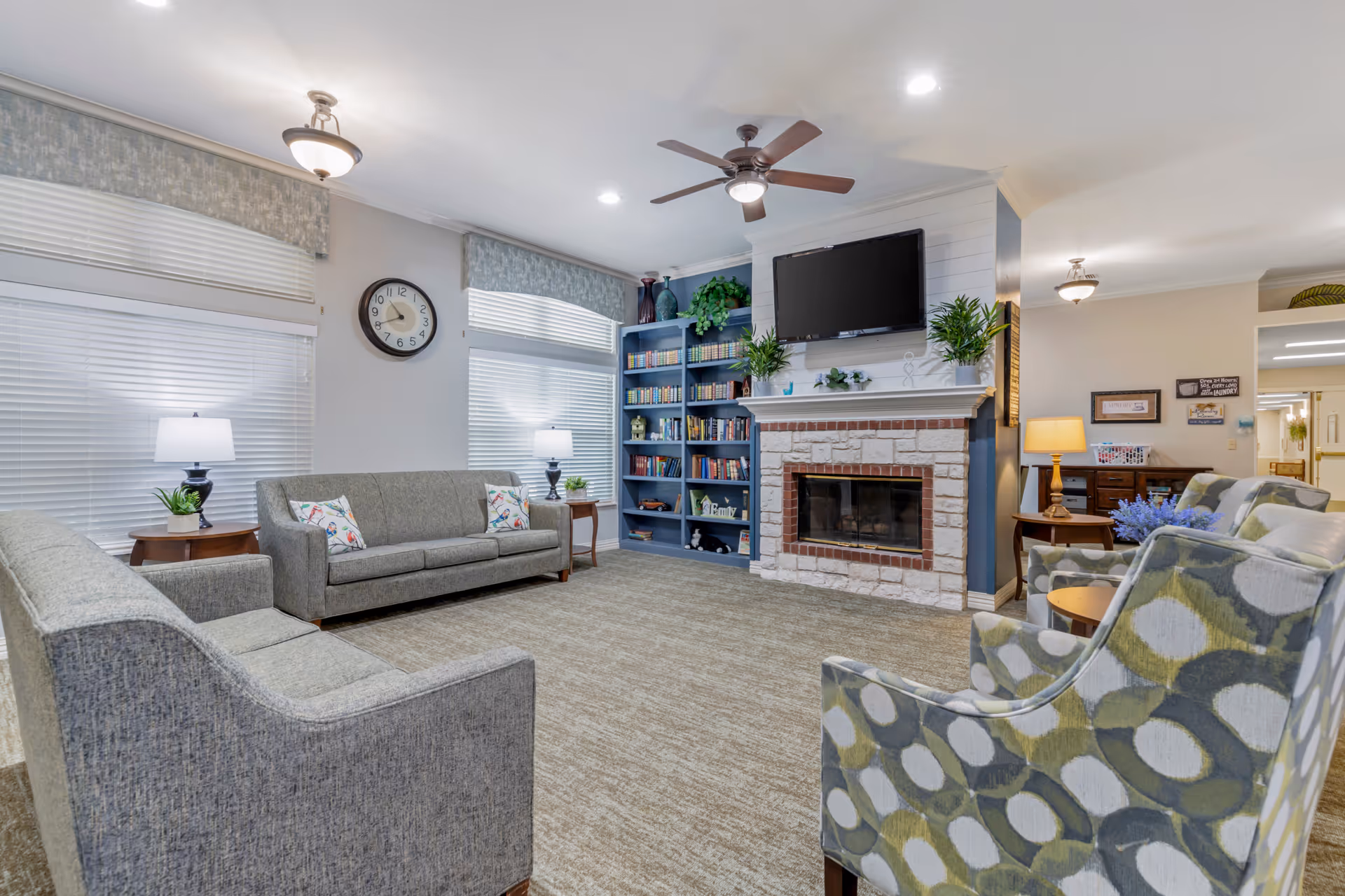 Cozy senior living living room with sofas, fireplace, bookshelves, and a wall-mounted TV.
