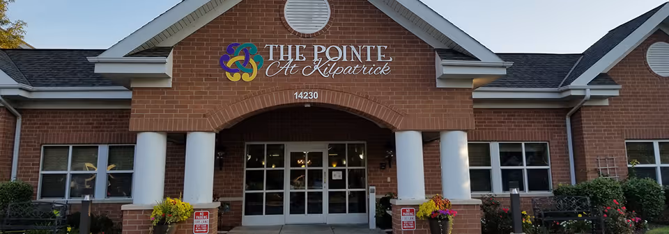 Front entrance of The Pointe At Kilpatrick senior living facility with brick facade, white columns, glass doors and signage.