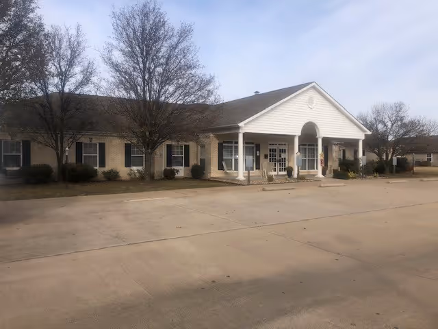 Carl Junction Residential Care Facility exterior: single-story building with a covered entrance and shrubs.