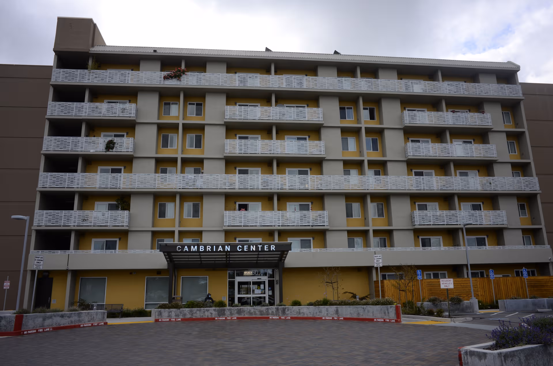 Multi-story senior living center with repeated balconies, labeled Cambrian Center, viewed from the parking lot.