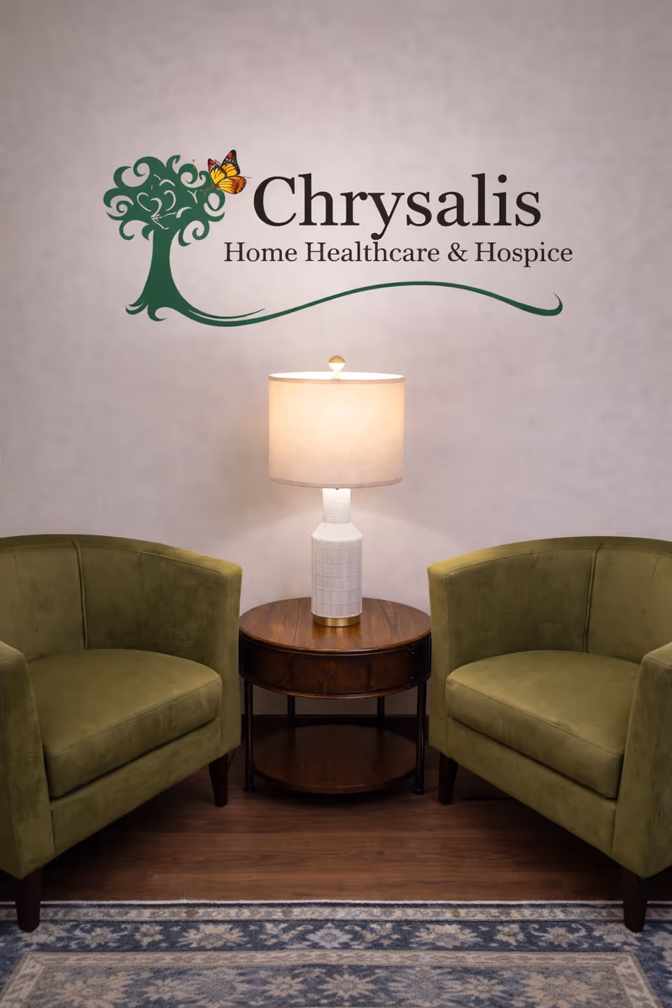 Lobby seating area with two green chairs, a lamp, and Chrysalis Home Healthcare & Hospice sign.