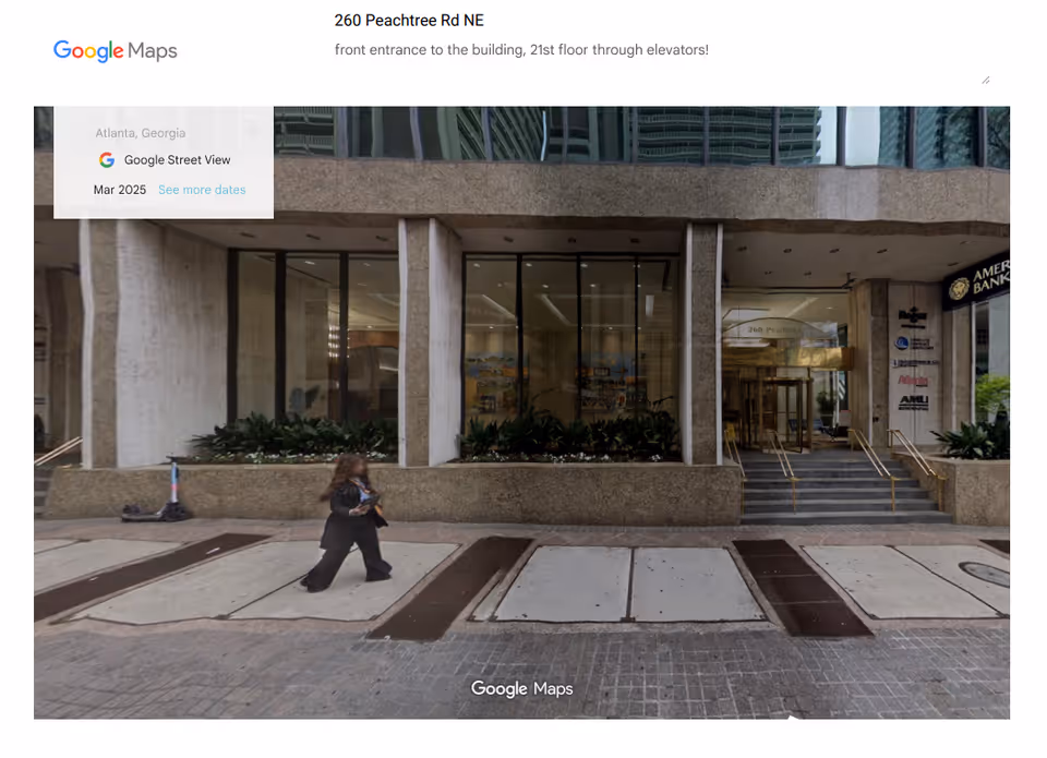 Front entrance of a tall building with glass doors, steps, plants, and a pedestrian walking.