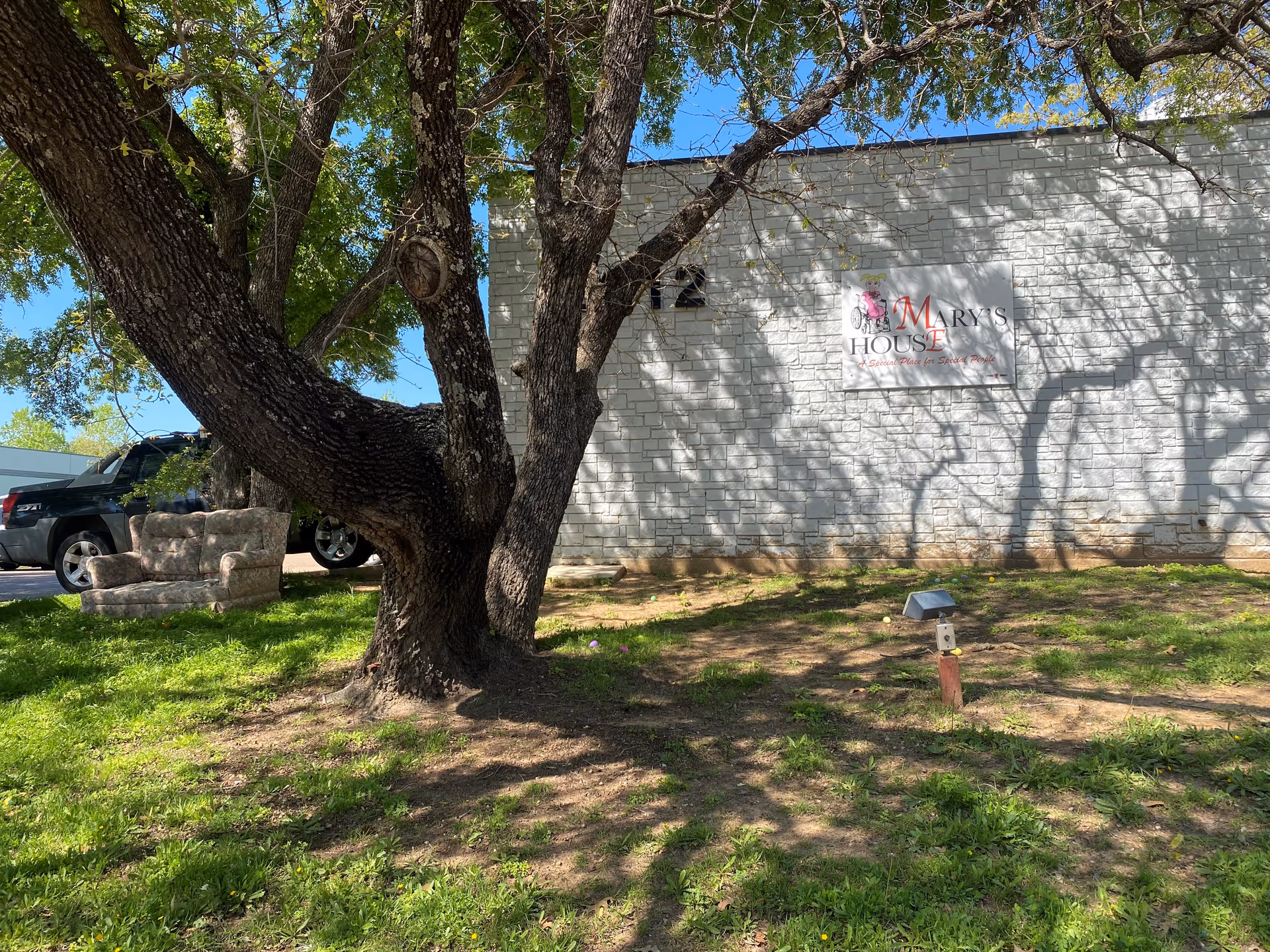 Large tree foreground with Mary’s House sign on a white brick exterior wall and parked truck