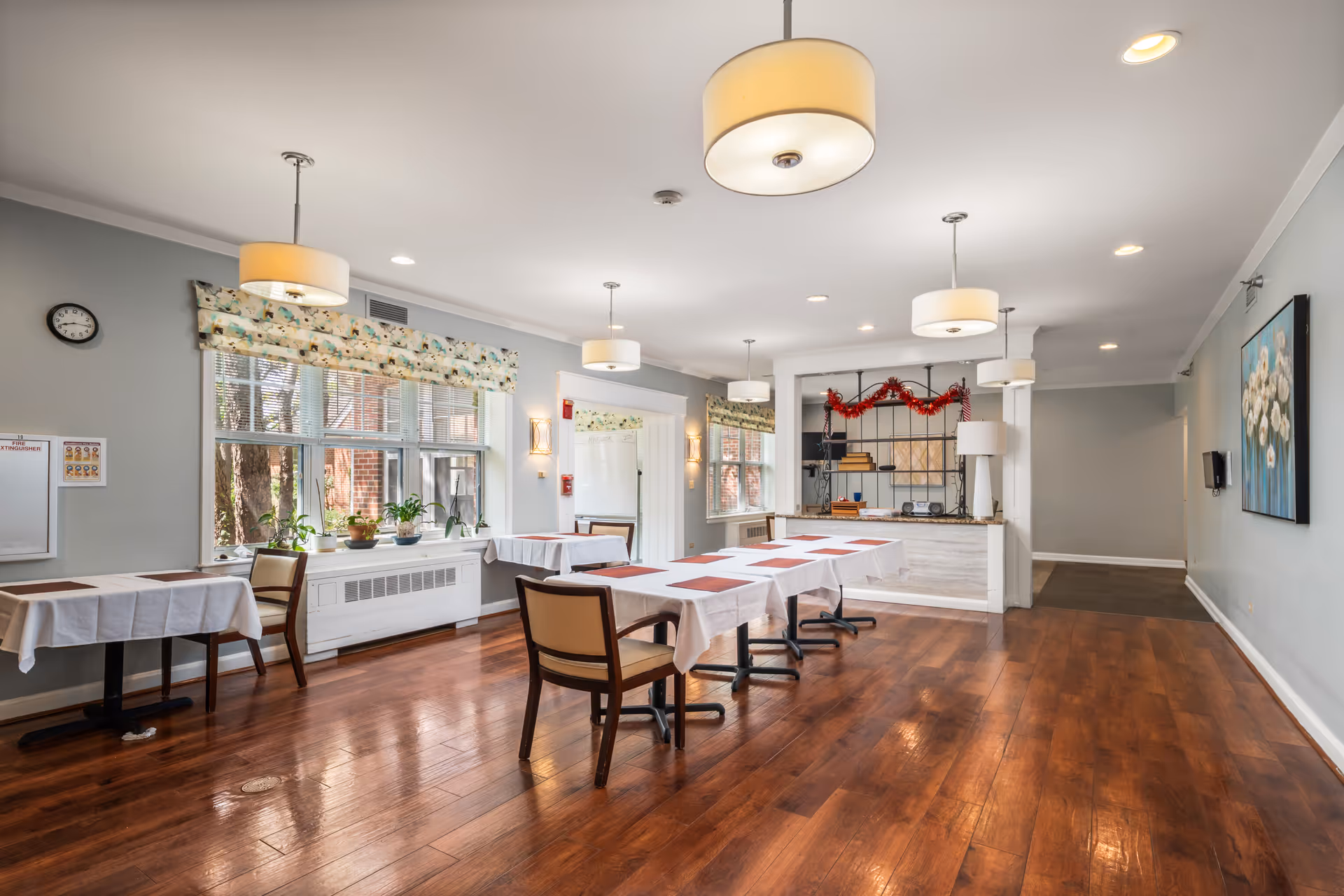 Bright dining room in a senior facility with long tables, chairs, and a reception desk.