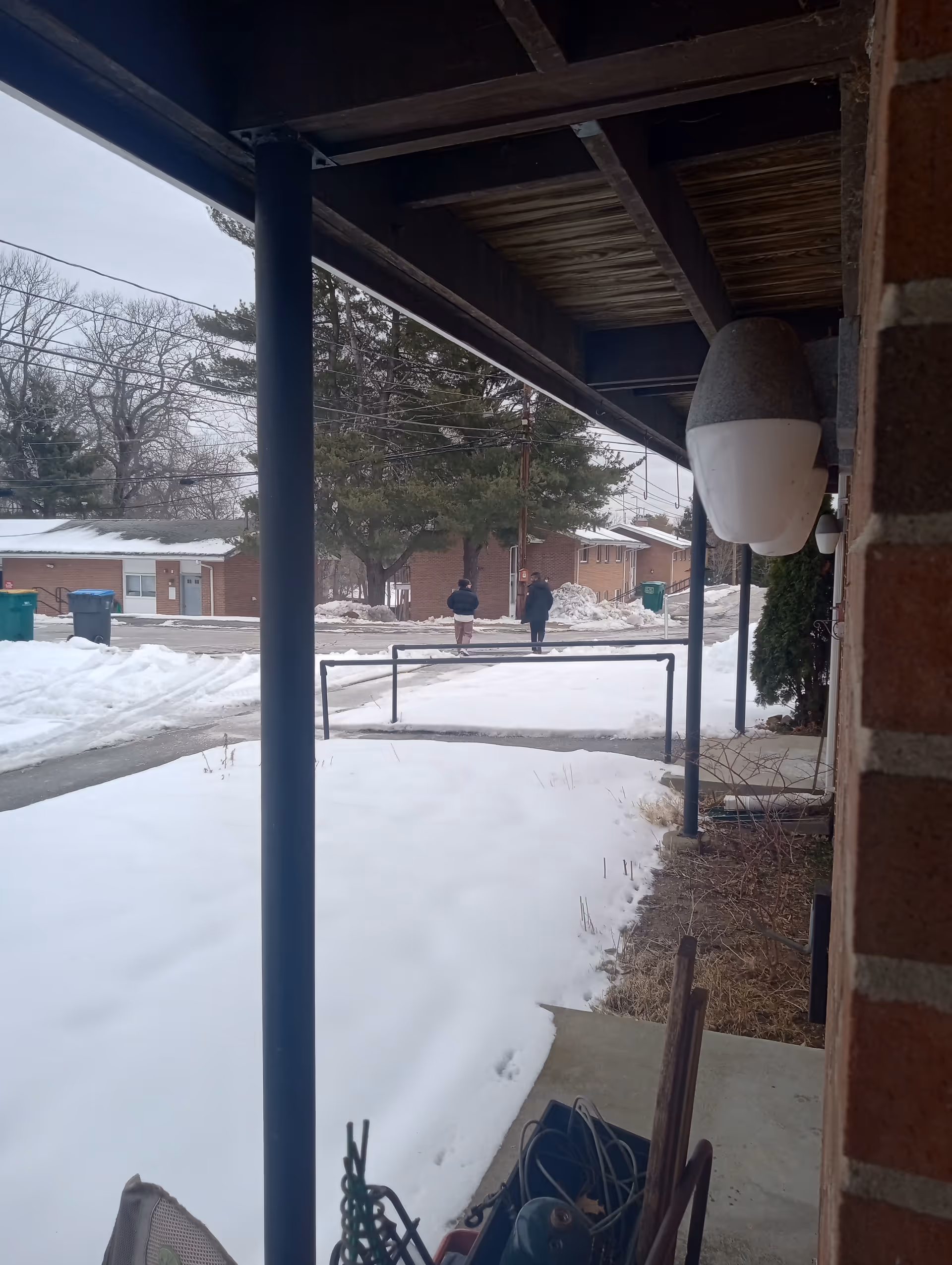 Covered exterior walkway with blue columns, snow on ground, and distant pedestrians.