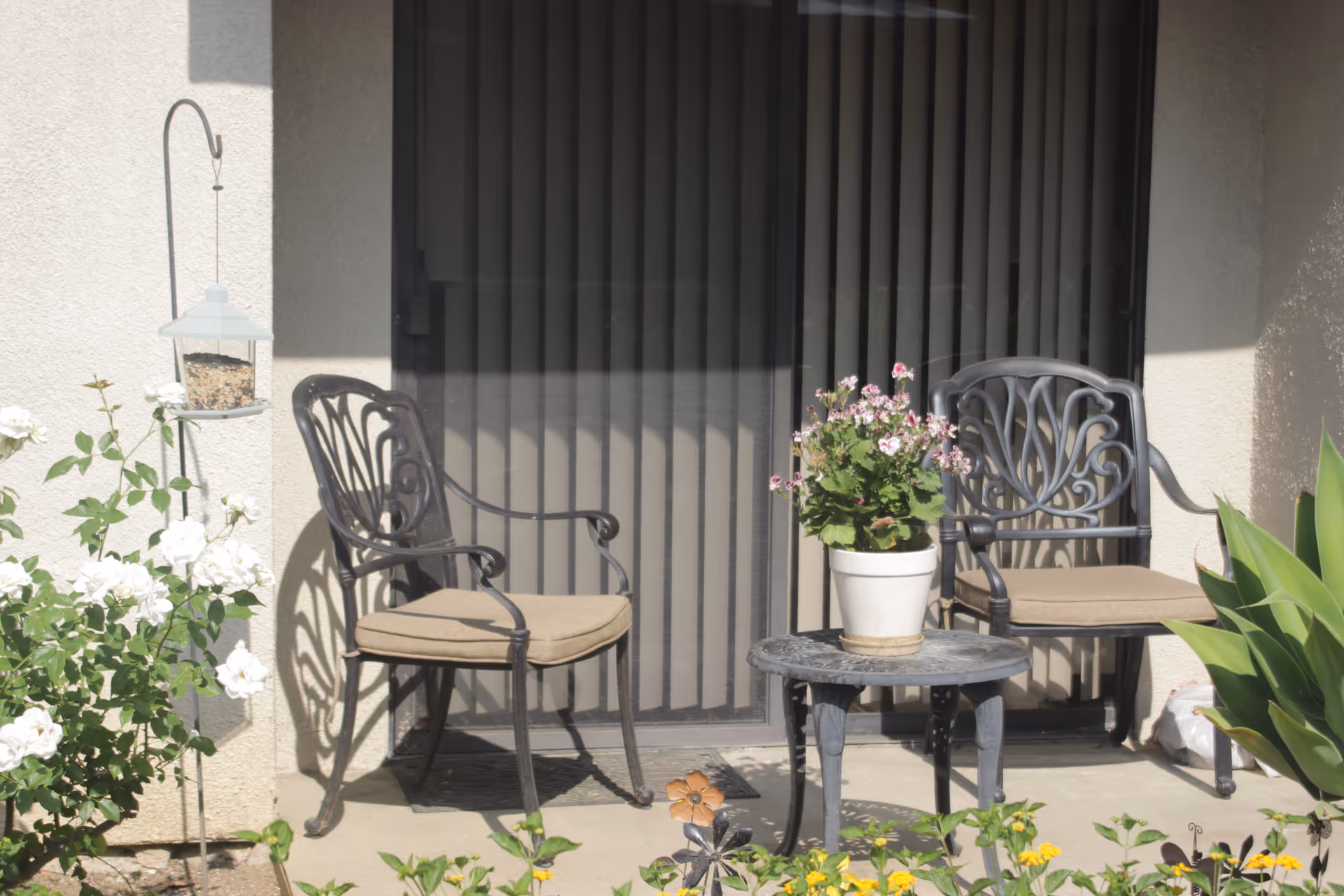 Front porch seating with two iron chairs, a small table, and potted plants.