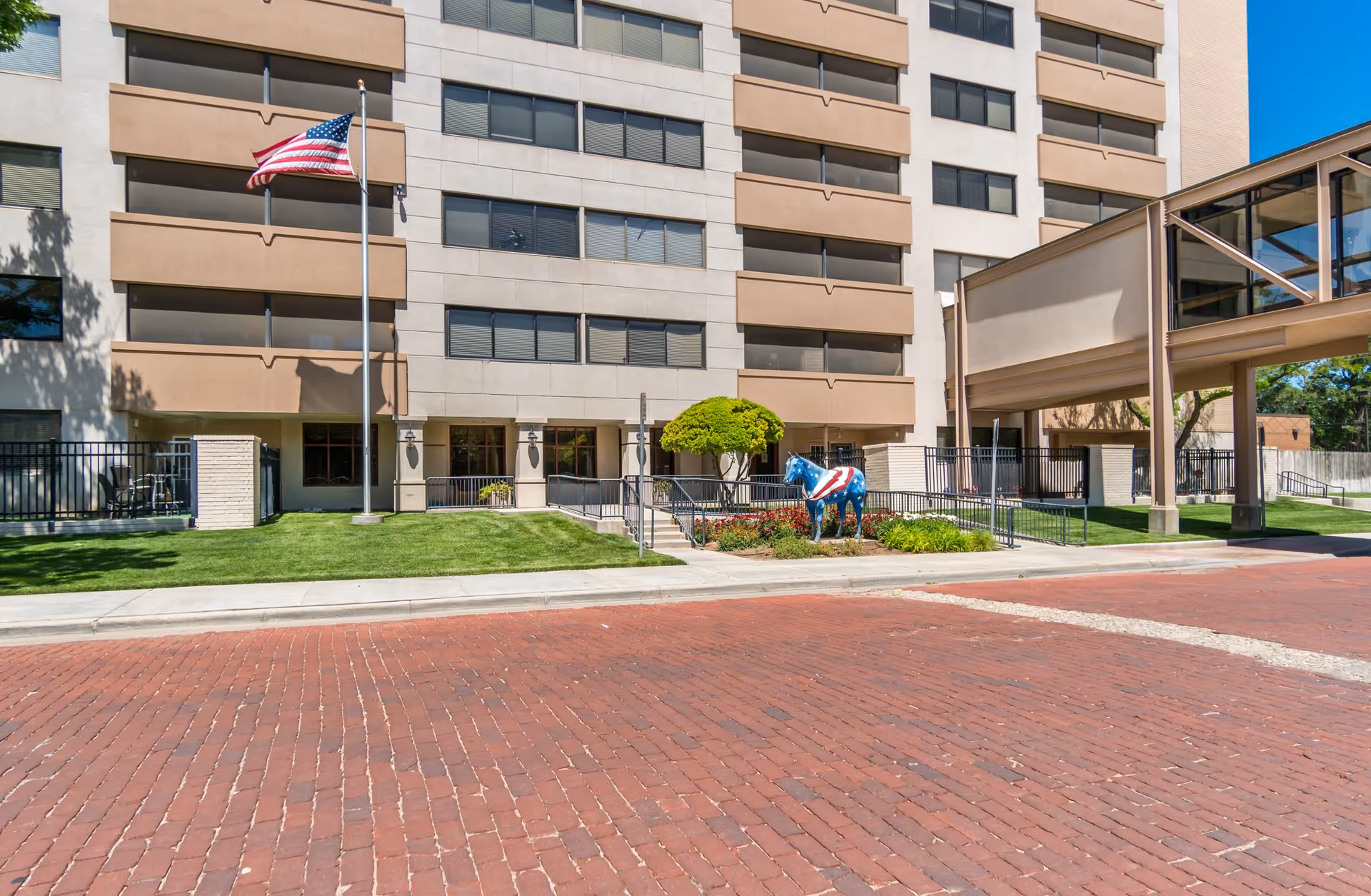Exterior view of The Continental senior living building with flagpole, lawns, and a decorative horse statue.