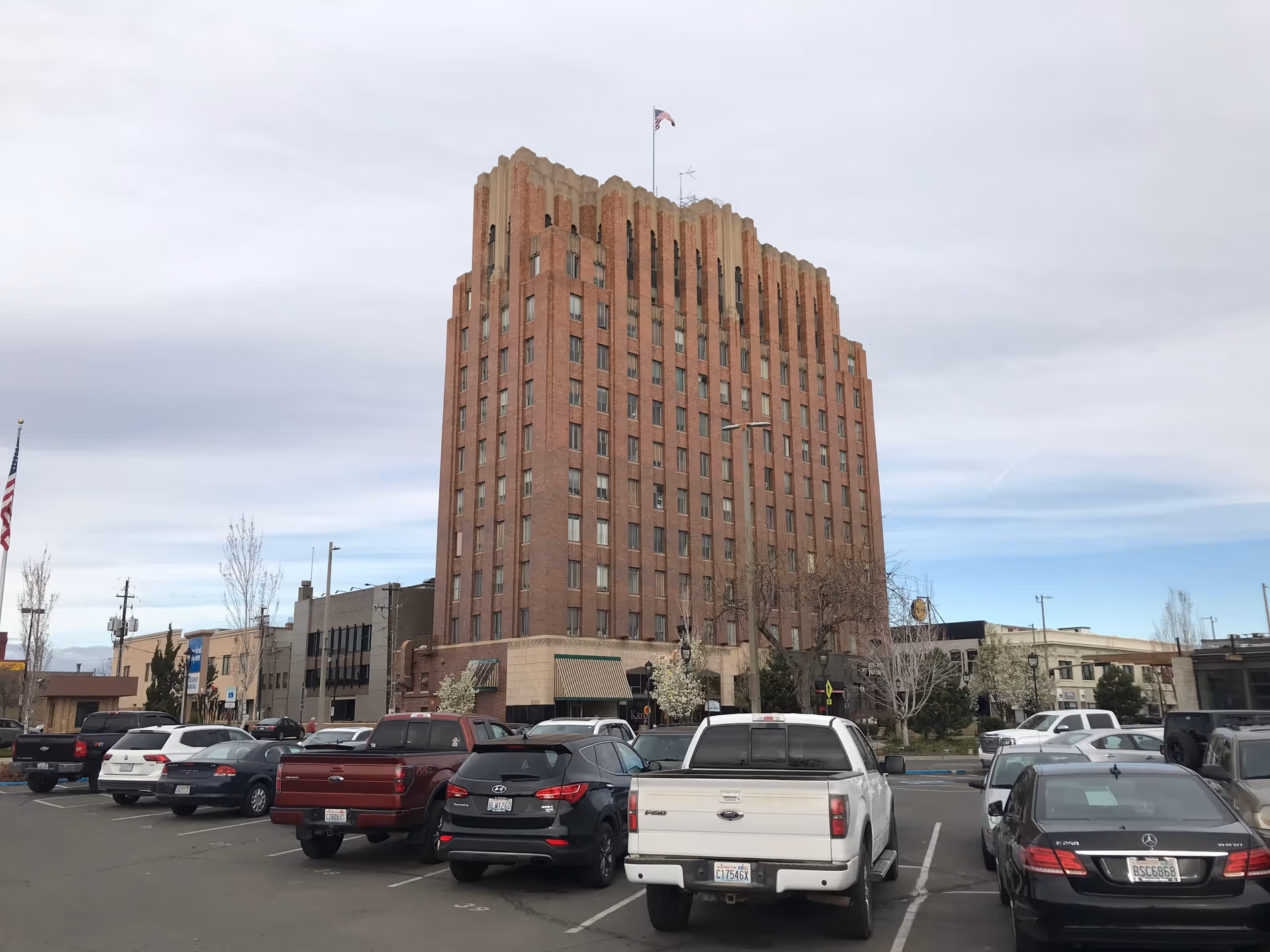 Tall brick building dominates the scene with a busy parking lot in front.