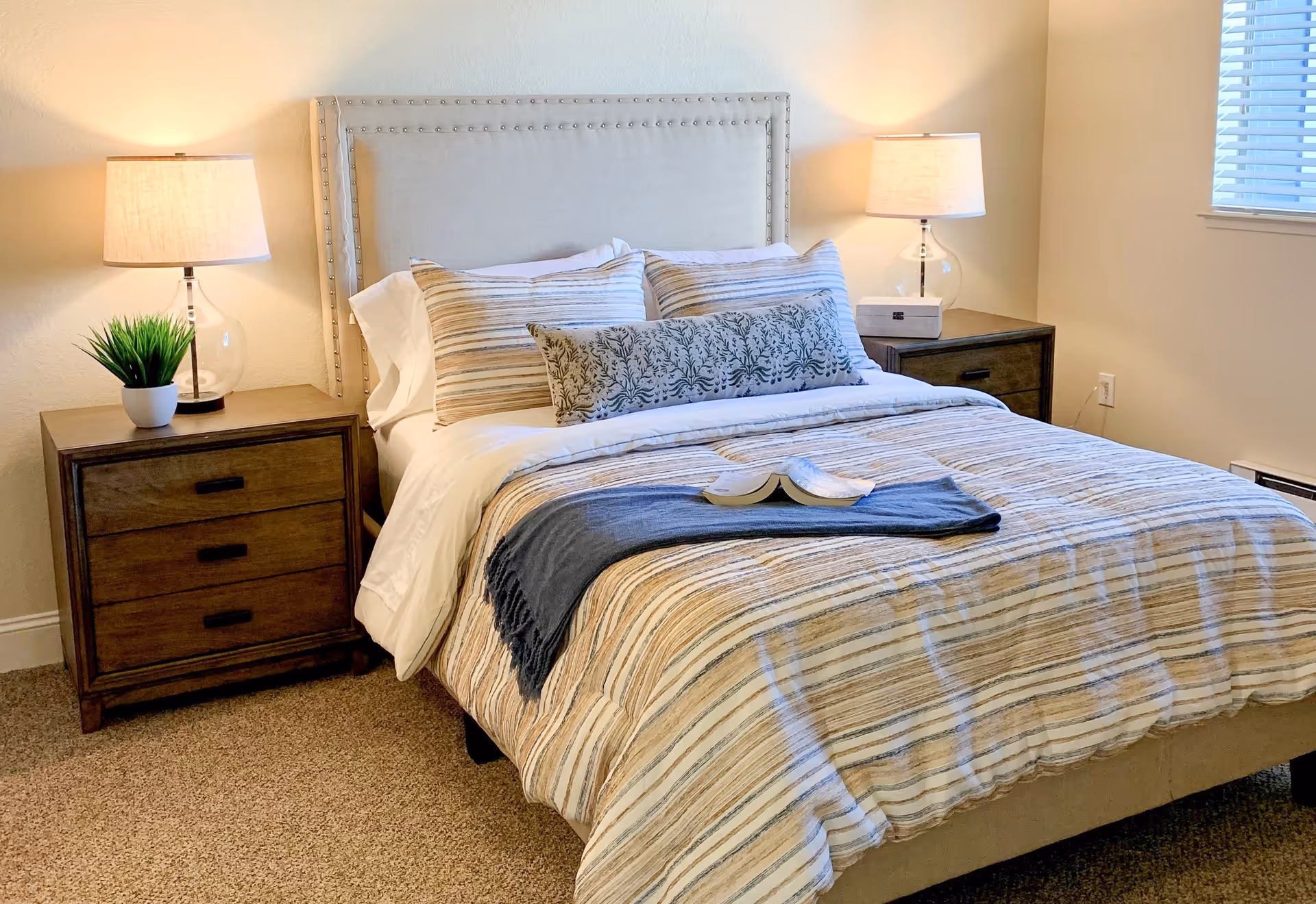 A neatly made bedroom with a striped comforter, two nightstands, lamps, and decorative pillows.