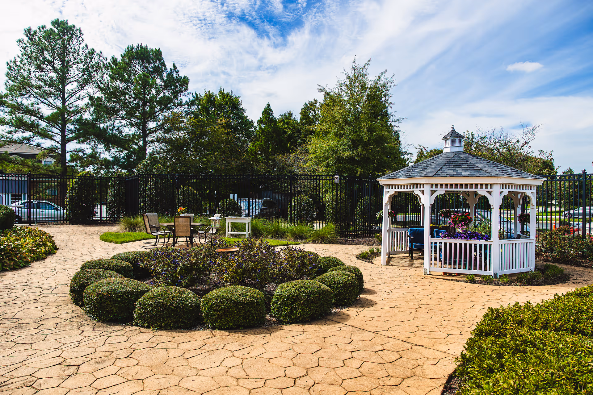 Well kept outdoor courtyard with a white gazebo, circular hedges, and patio seating.