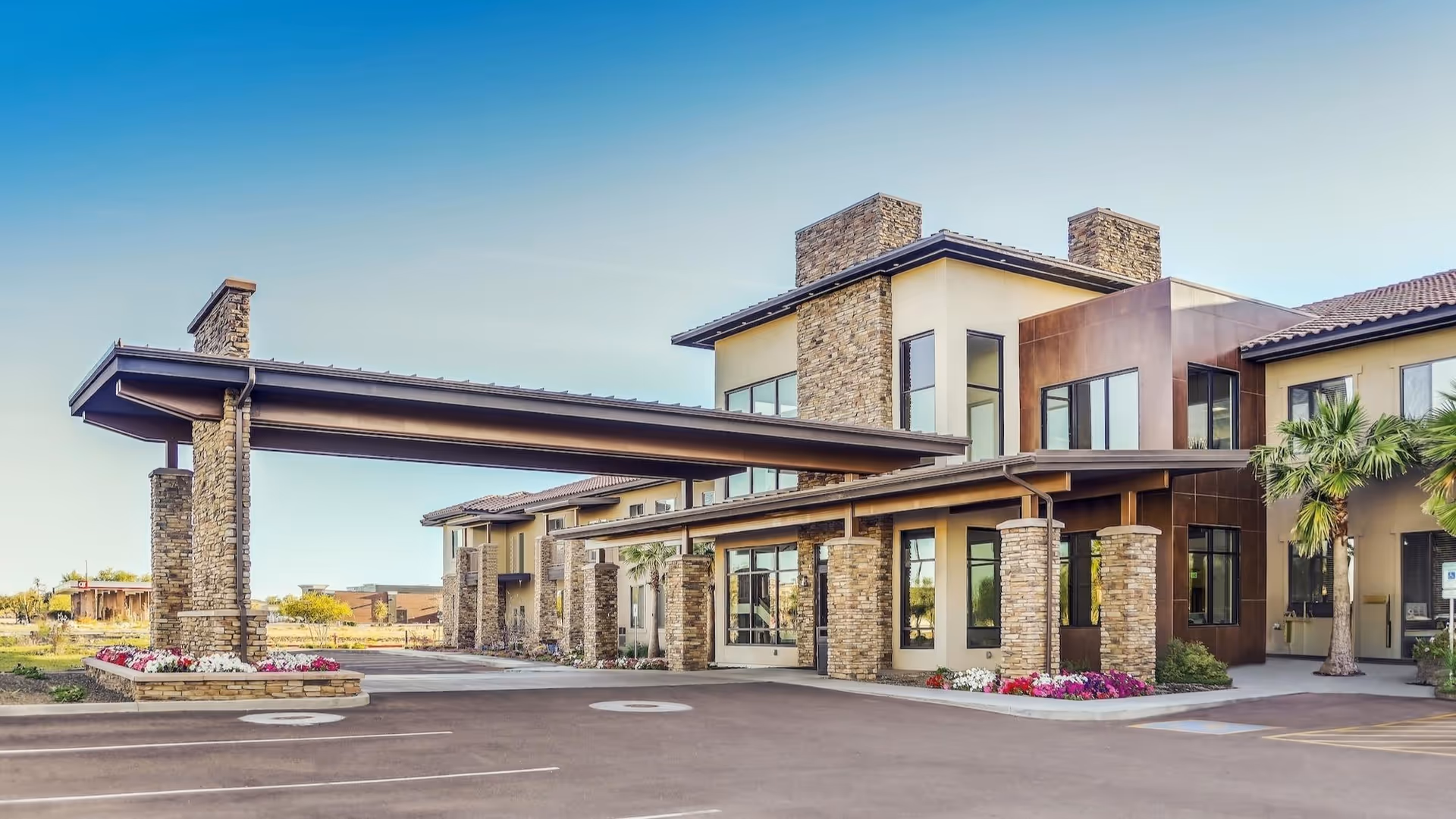 Modern senior living facility exterior featuring stone pillars, a covered entrance, and landscaped surroundings.
