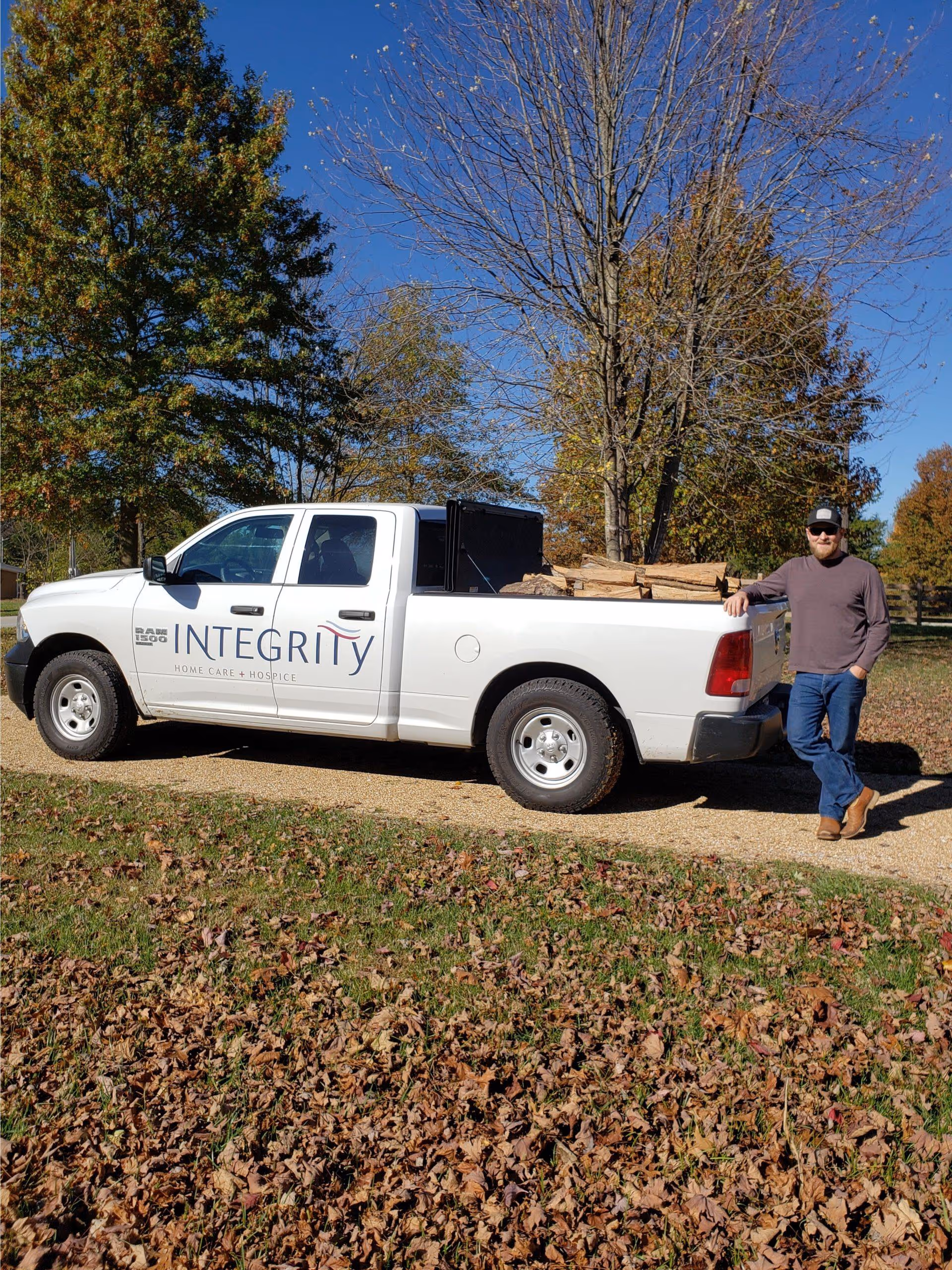 White pickup truck branded Integrity parked on a dirt path; man leans at tailgate with wood.