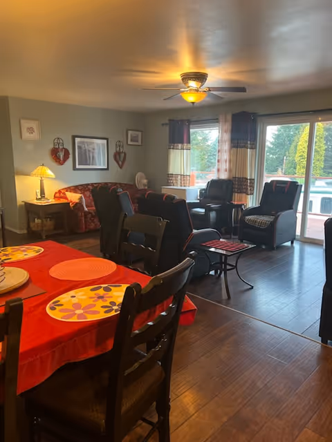 Cozy senior living dining area with red tablecloth, chairs, and connected living space.
