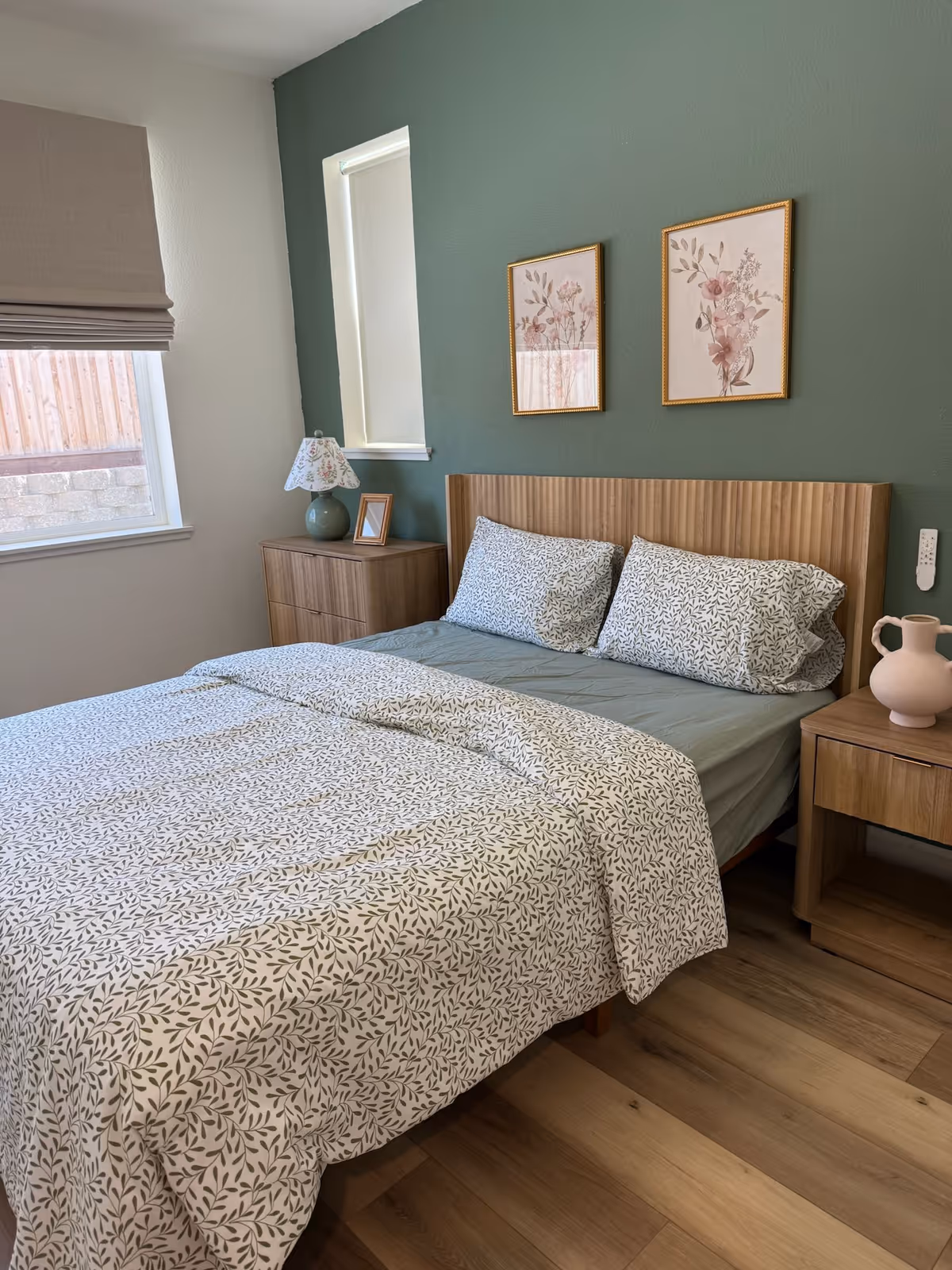 A neatly made bedroom with a wooden bed, nightstands, lamps, and framed art.