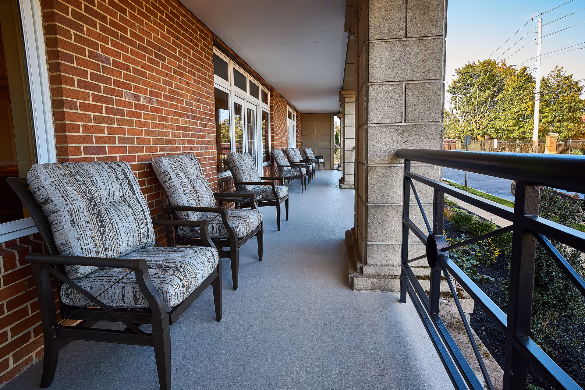 Outdoor corridor with cushioned chairs along brick wall and railing.