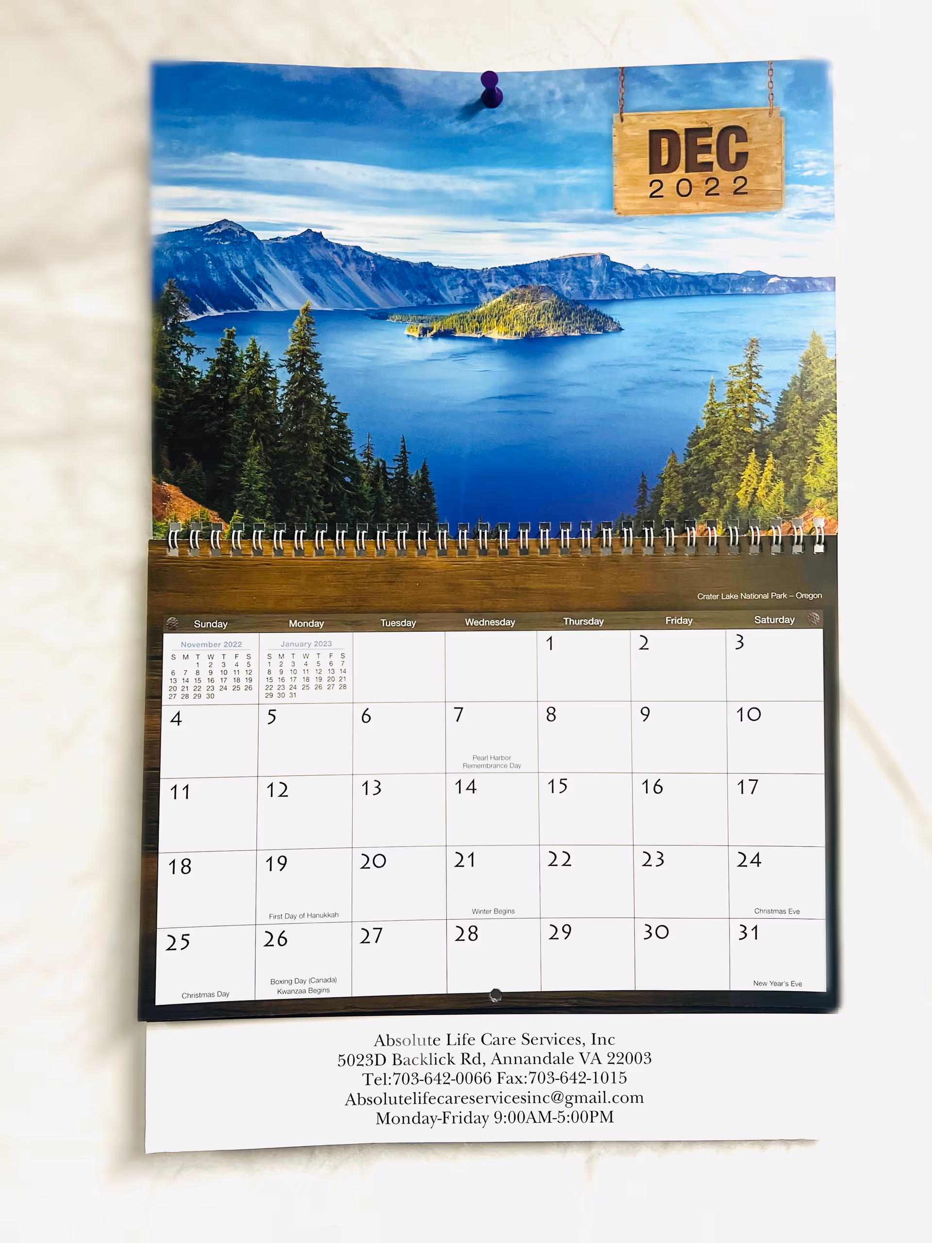 Indoor wall calendar featuring a mountain lake photo above a monthly grid and contact details.