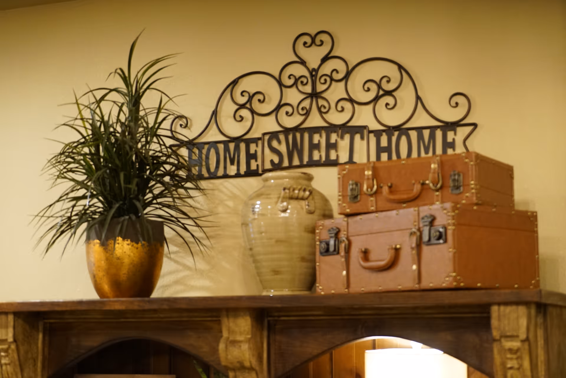Interior decor on shelf with plant, vase, and vintage suitcases beneath a Home Sweet Home sign