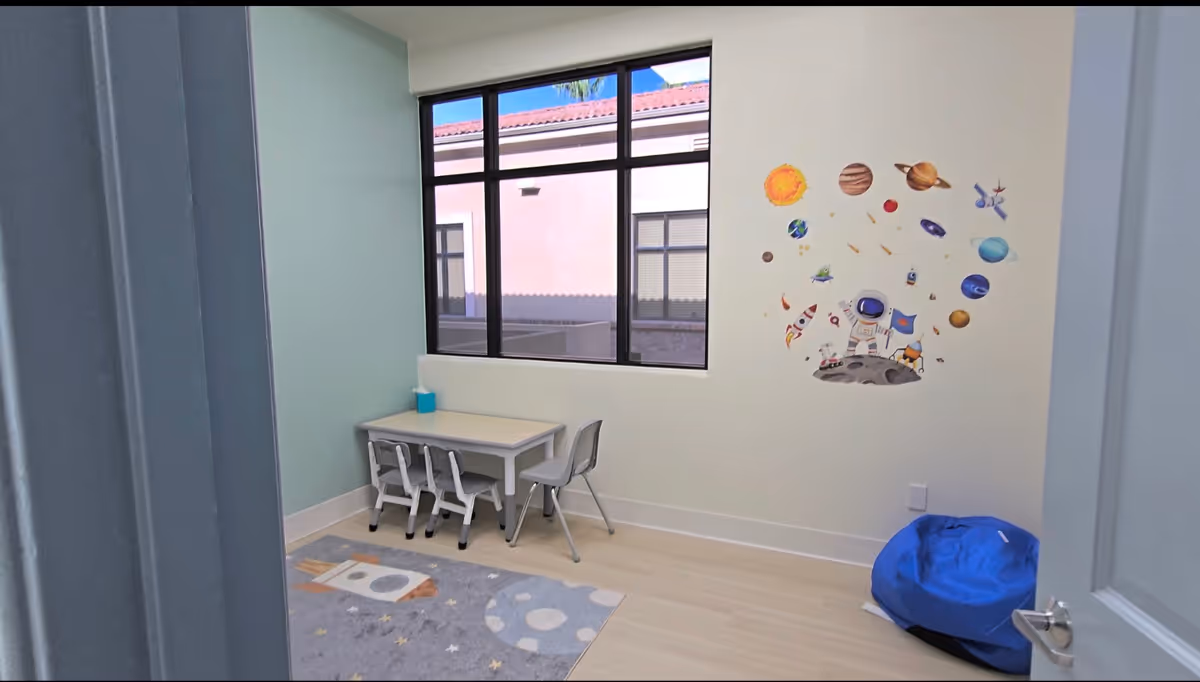 Small activity room with a table, chairs, rug, and space-themed wall decals.