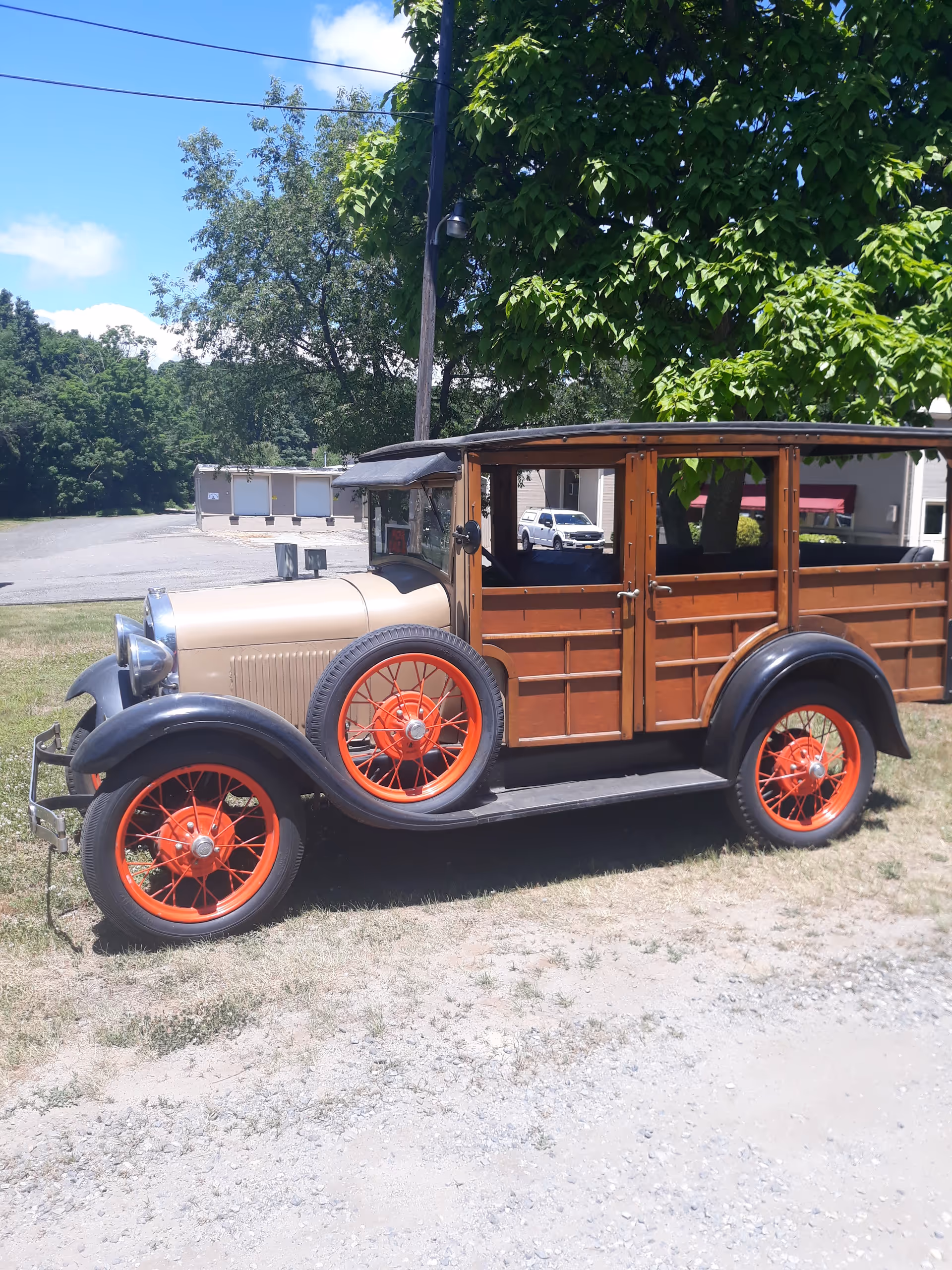A vintage wooden-bodied car with red-spoked wheels is parked on grass.