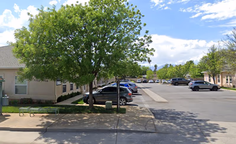 A driveway and parking lot outside a single-story senior care facility with trees and cars.