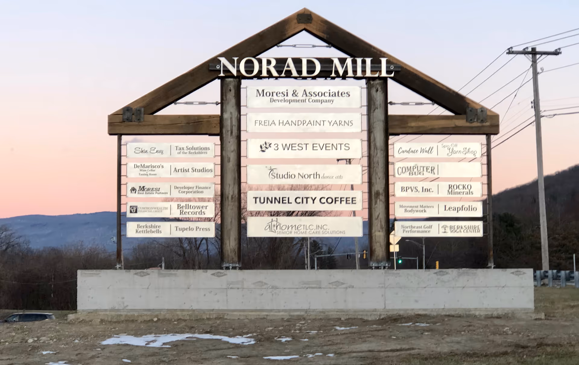 Large wooden-framed outdoor sign with numerous business panels at Norad Mill.