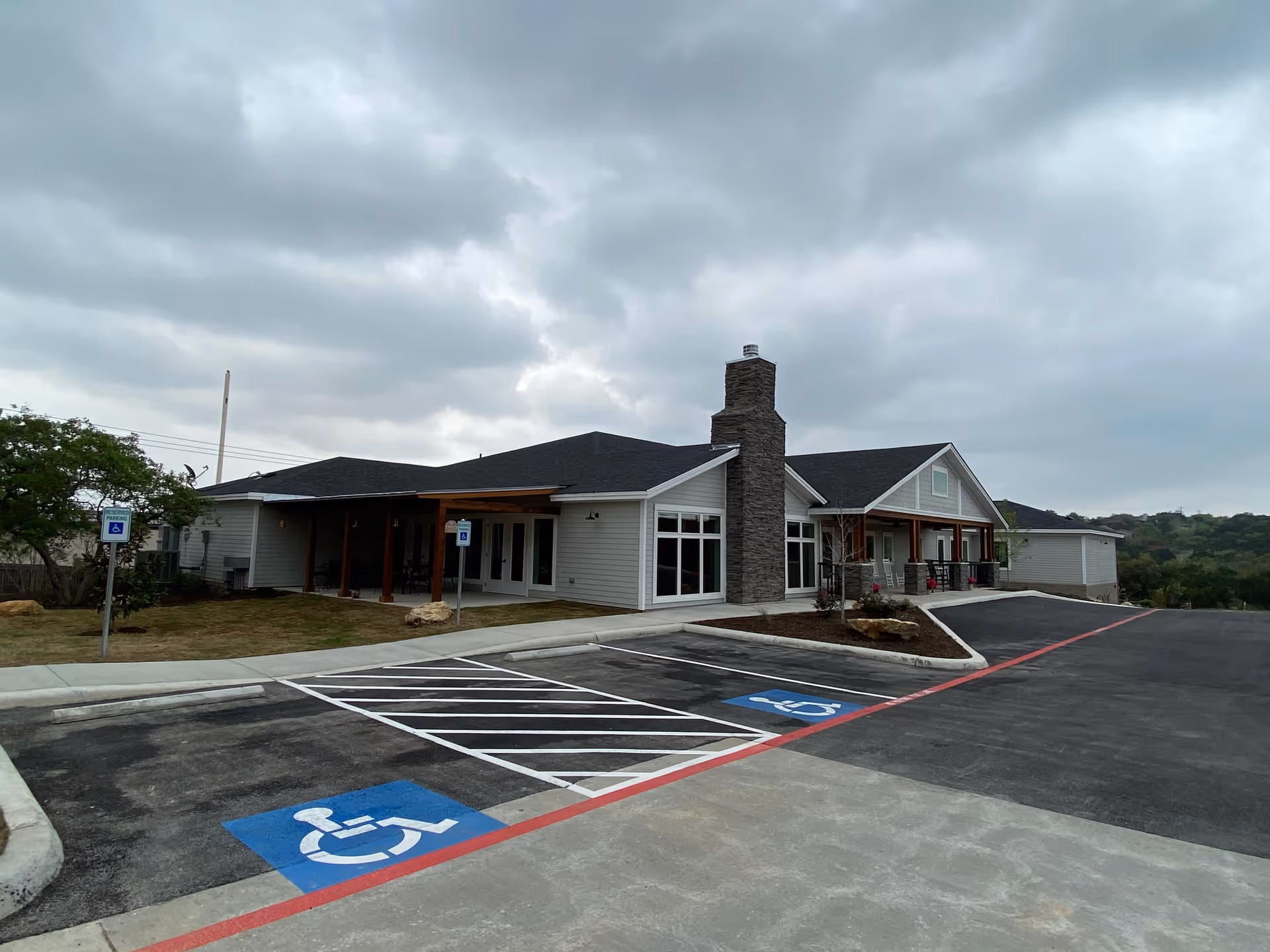 Single-story assisted living facility with a stone chimney, covered entrance, and handicapped parking.