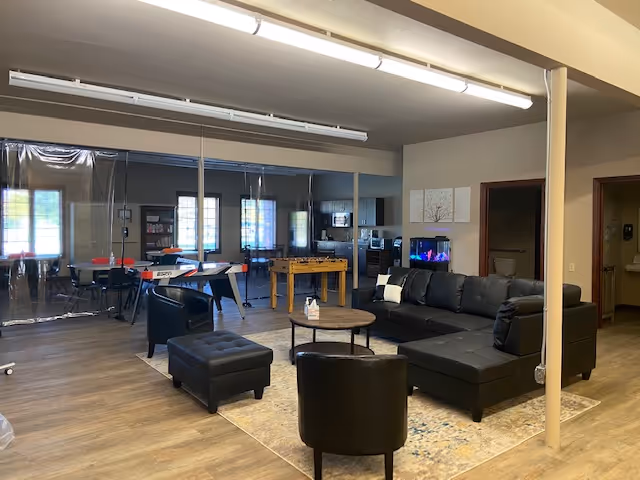 Spacious common lounge with black sectional sofa, coffee tables, and rugs.