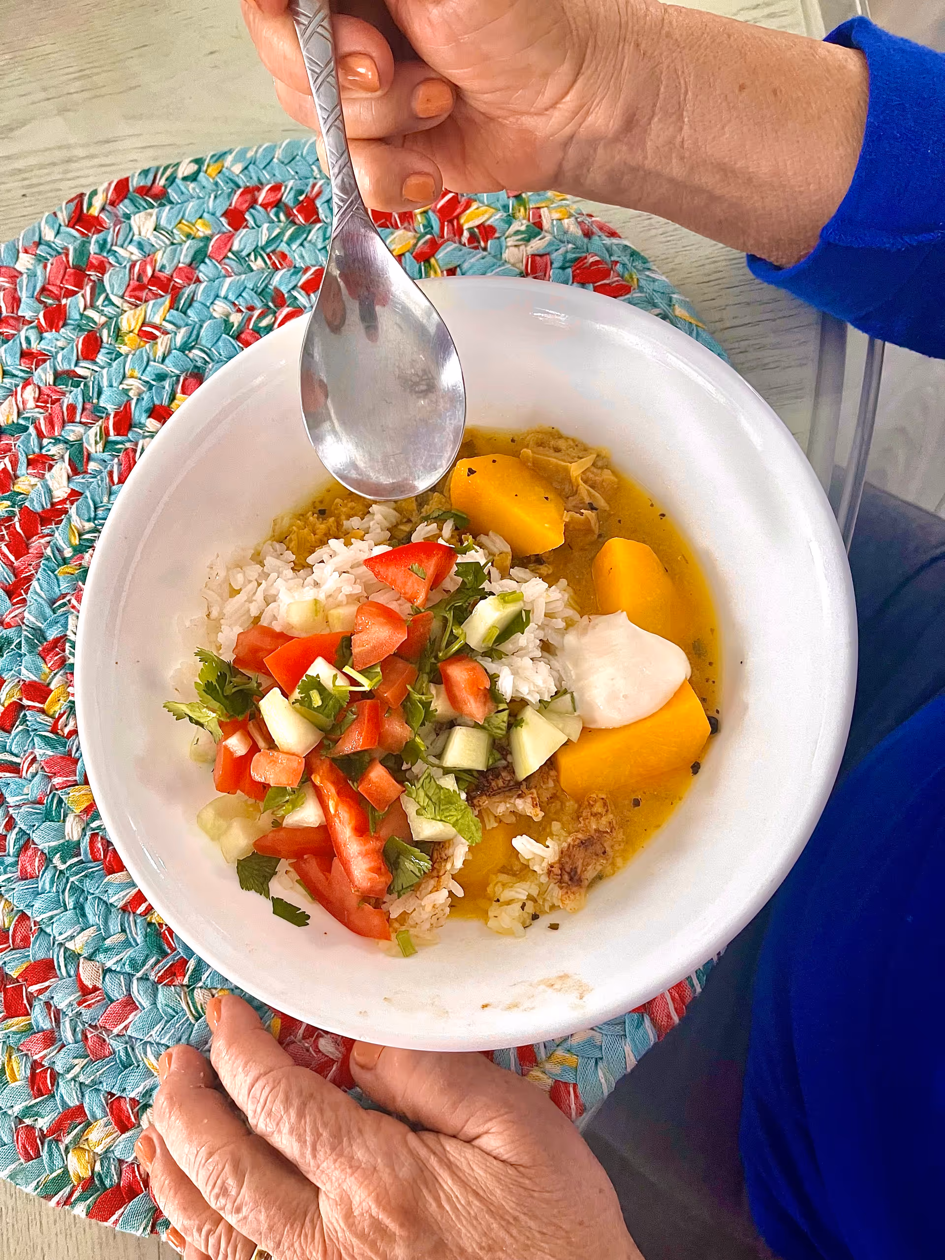 An elderly person’s meal in a bowl with rice, vegetables, and sauce on a colorful placemat.