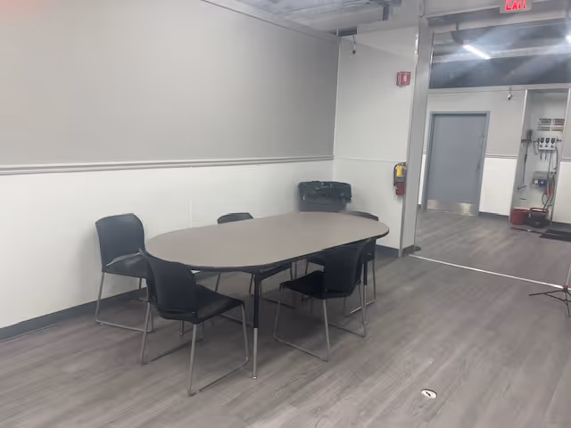 A plain conference room with an oval table and black chairs.