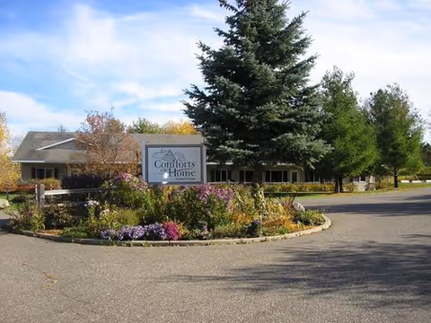 Exterior view of Comforts of Home facility with flower garden, sign, and driveway.