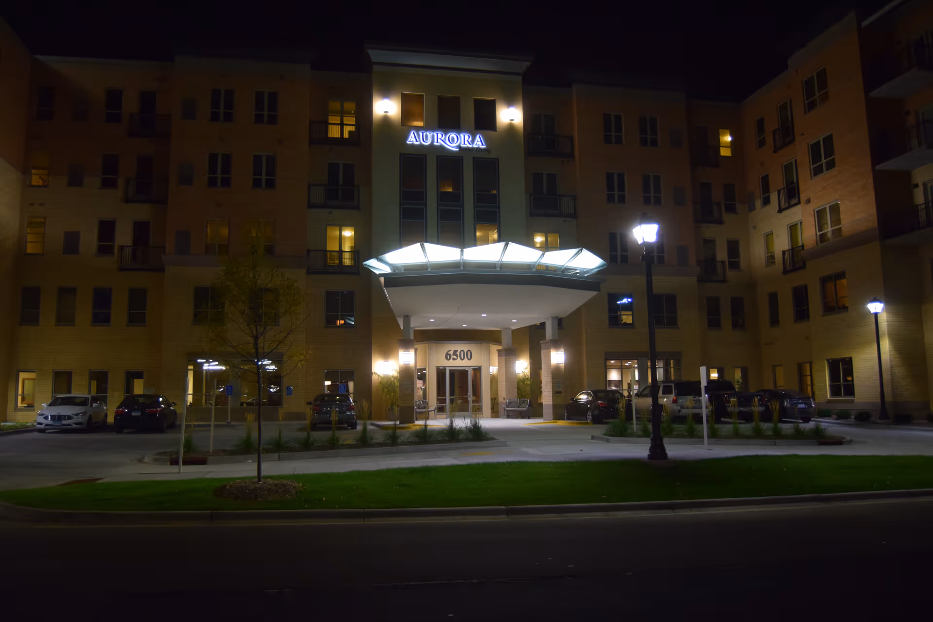 Night exterior view of Aurora on France senior living building with lit entrance canopy and cars.