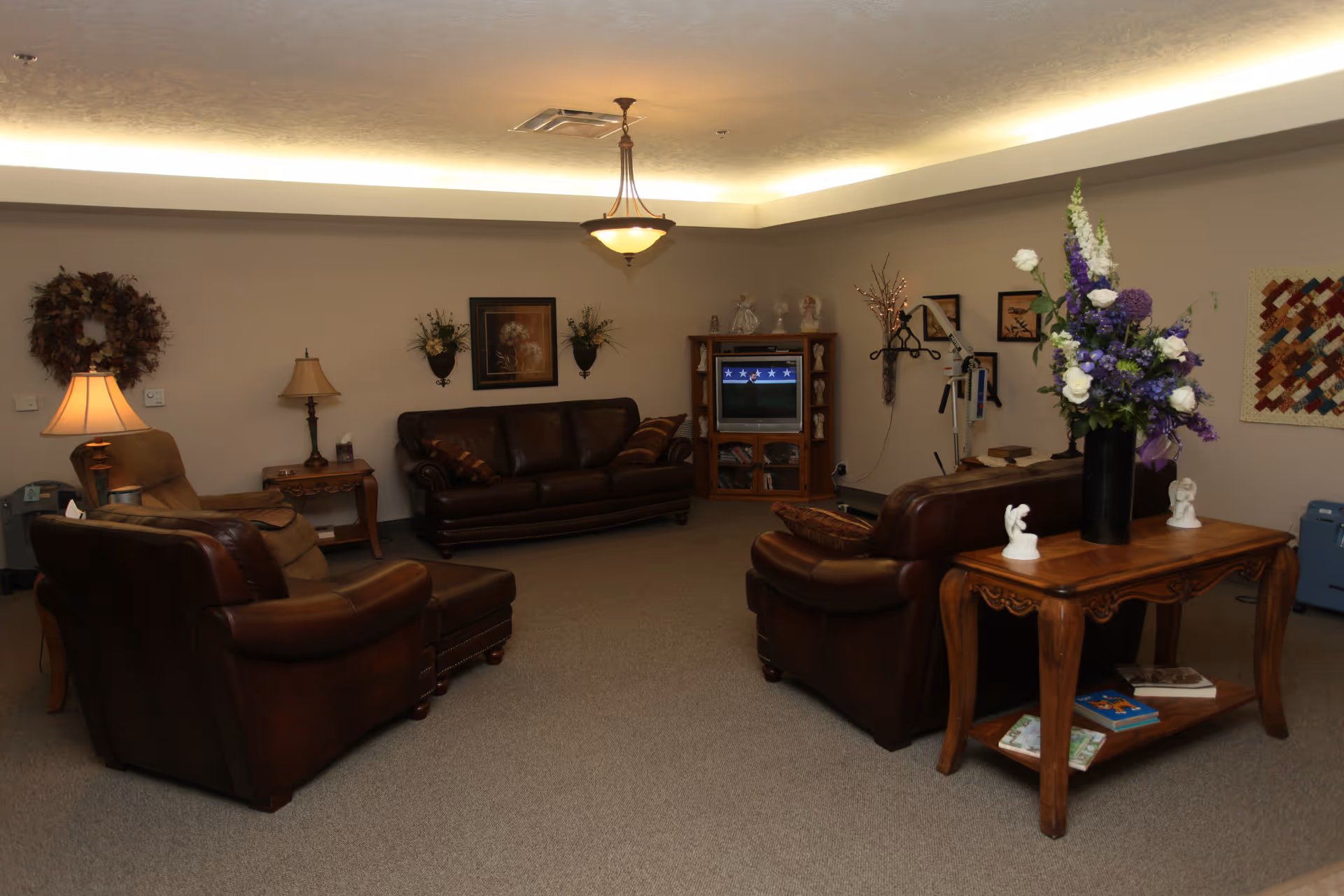 A cozy, well-lit senior living room with leather sofas, a TV, and floral decor.