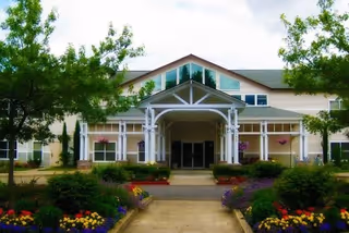 Sunlit senior living building with a covered entrance and colorful flower beds.